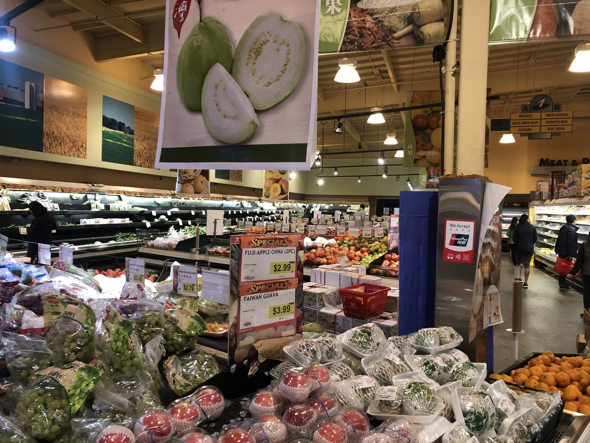 Produce bins at 99 Ranch Market in Foster City, under a hanging sign of cut guava
