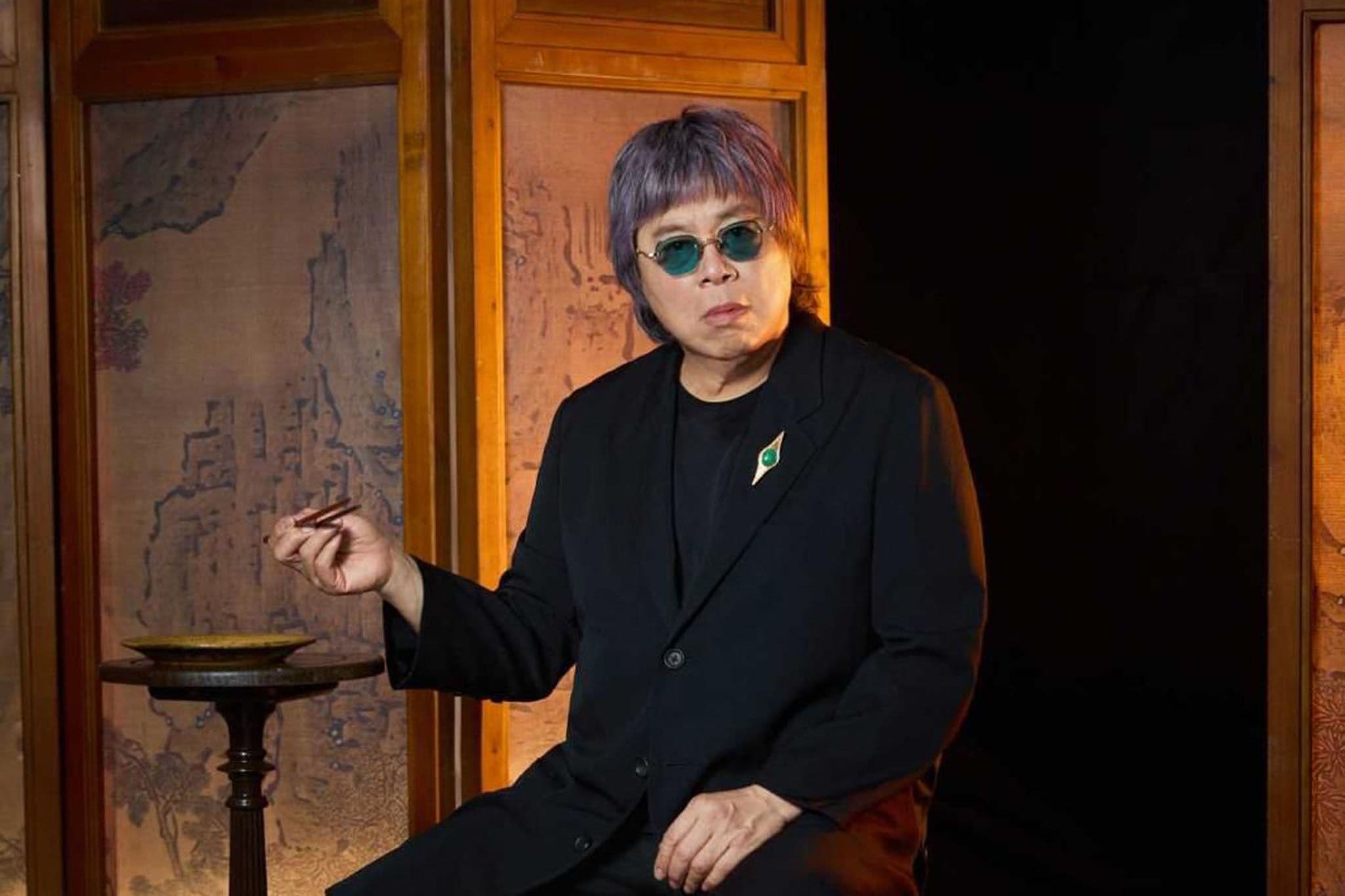 Chef Alvin Leung seated with chopsticks beside a Chinese folding screen