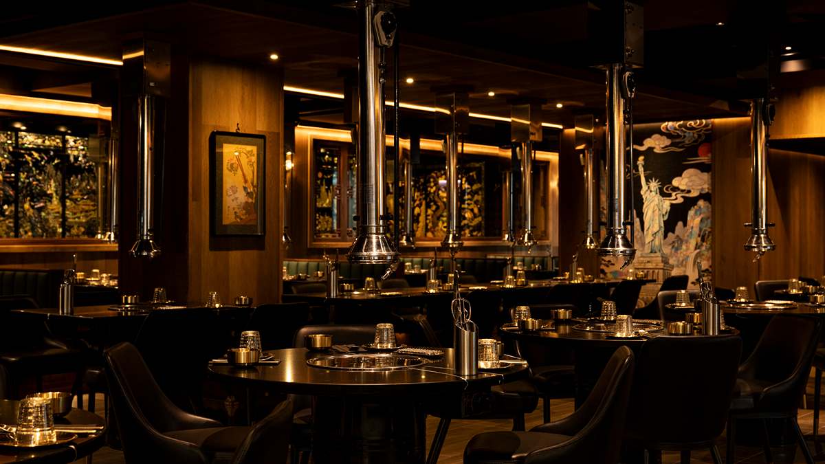 An empty dark dining room at Baekjeong Black, with steel exhaust hoods over black grill tables and a painted Statue of Liberty on the far wall