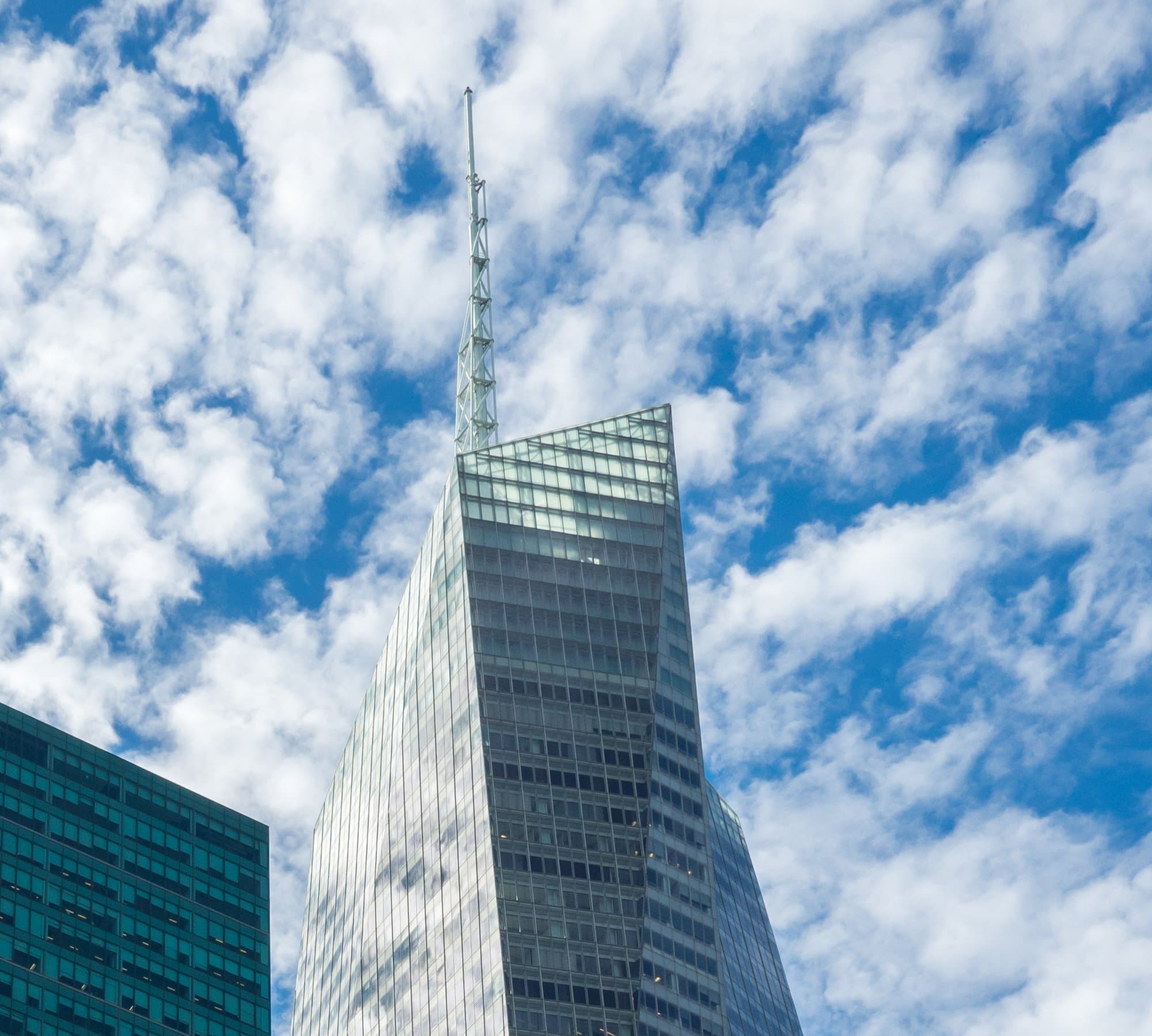 Glass crown of the Bank of America Tower against a blue sky with scattered clouds, seen from Bryant Park