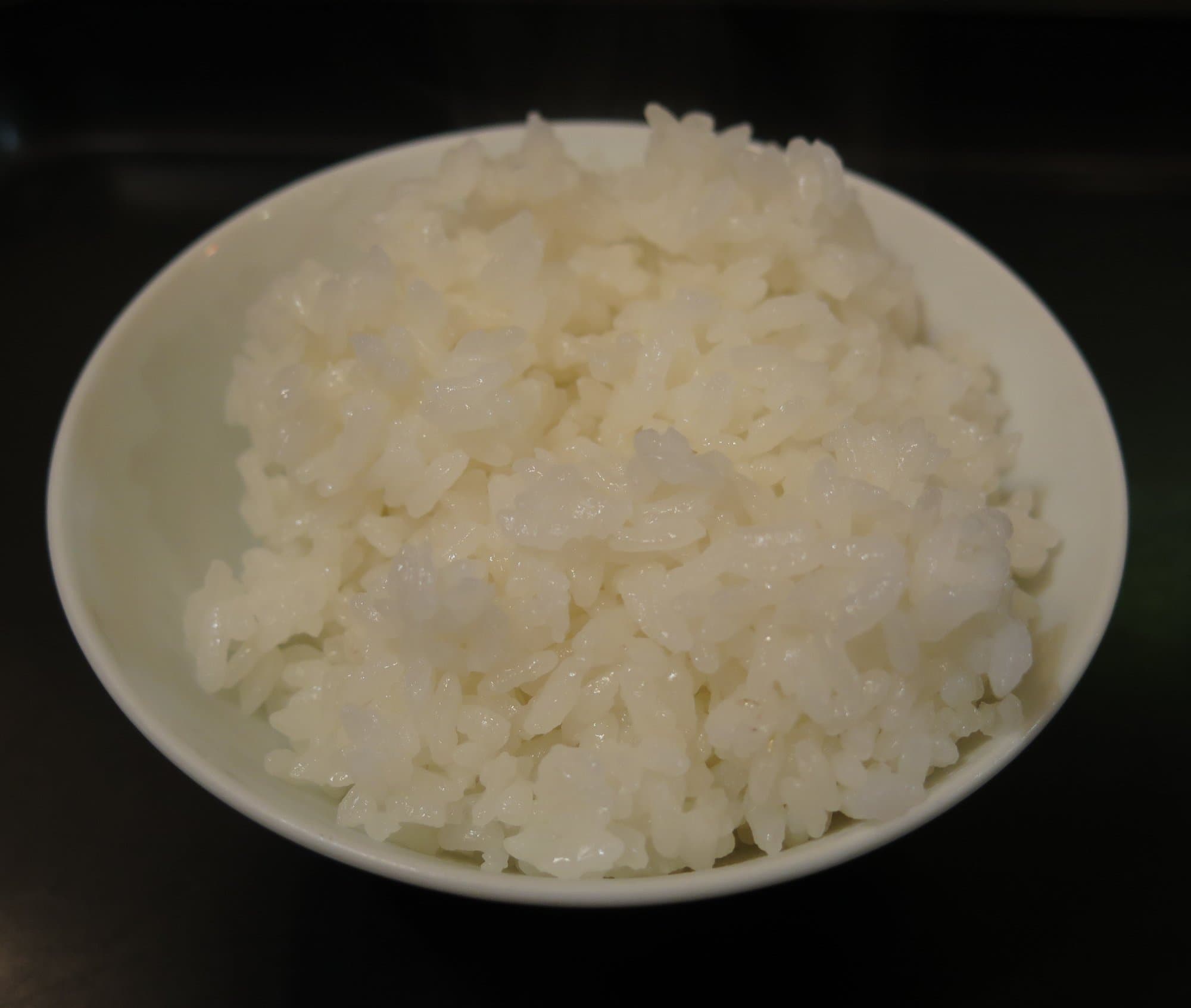 A white bowl heaped with glossy cooked rice, grains still separate, on a dark table