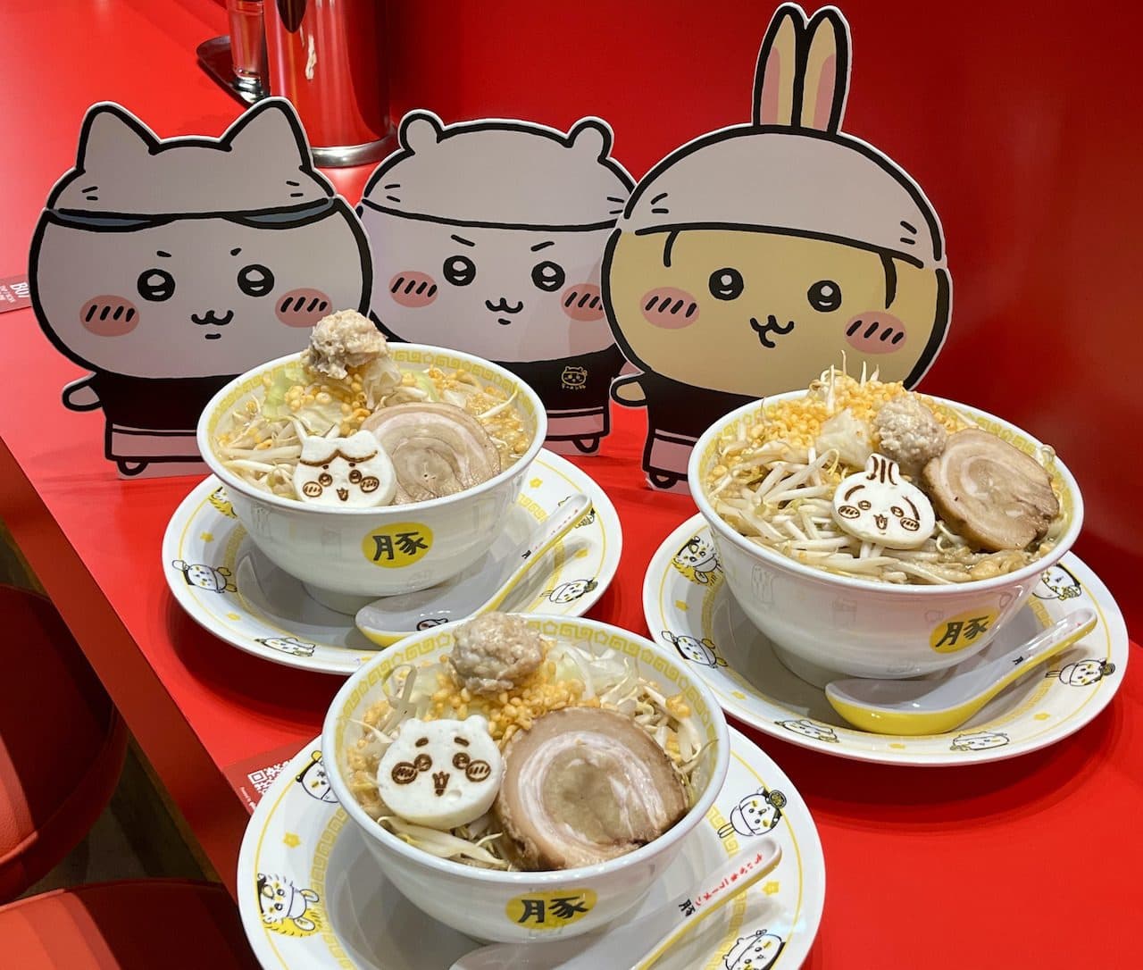 Three Chiikawa Ramen Buta bowls with character fish cakes and character standees behind them