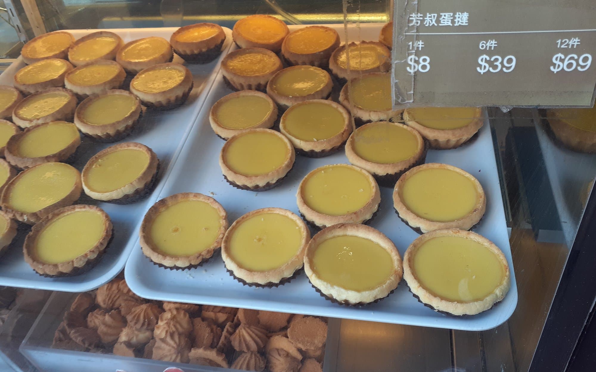 Bakery case trays of Hong Kong–style egg tarts with price labels