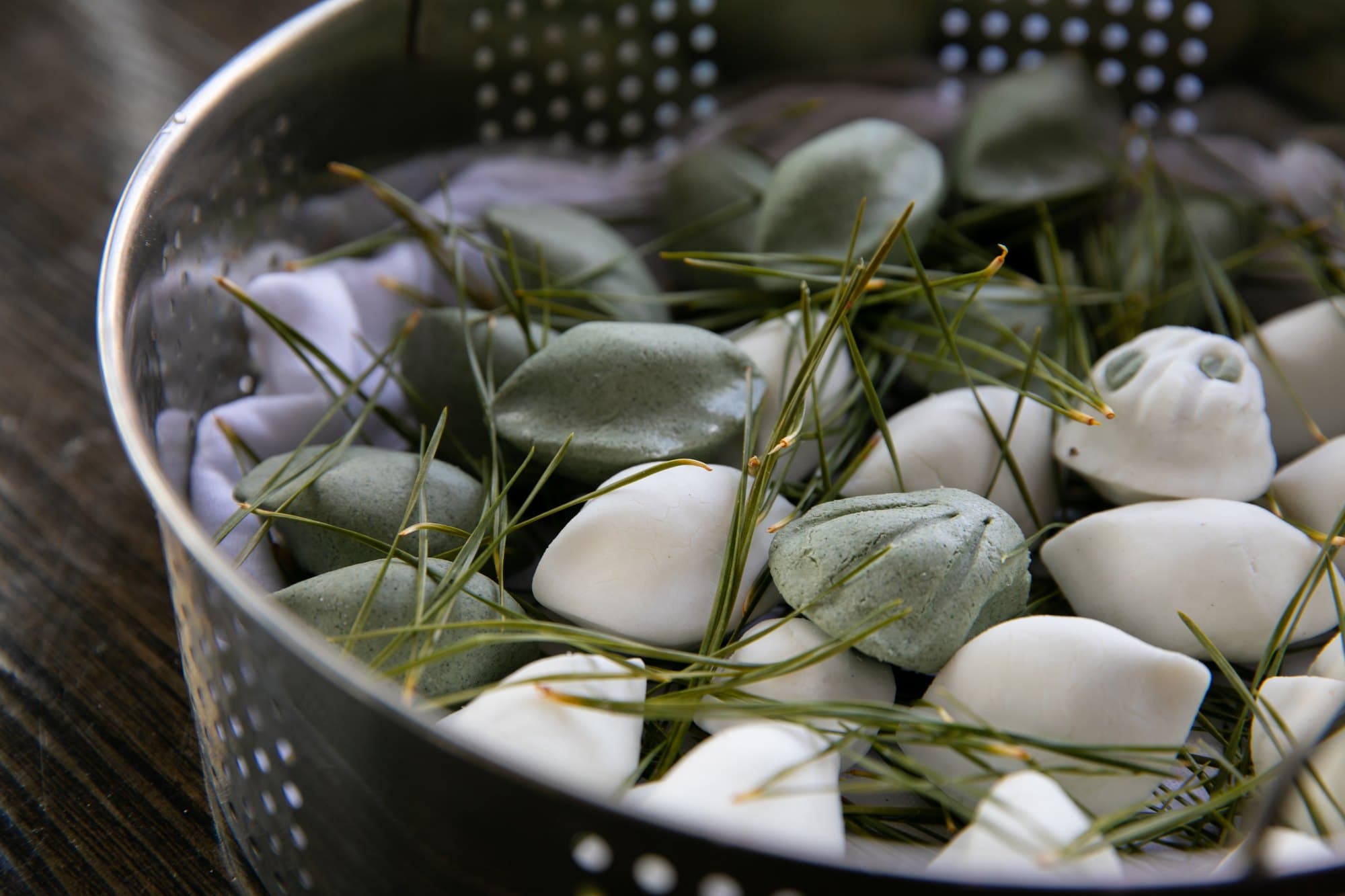 White and mugwort-green half-moon songpyeon resting on pine needles in a metal steamer