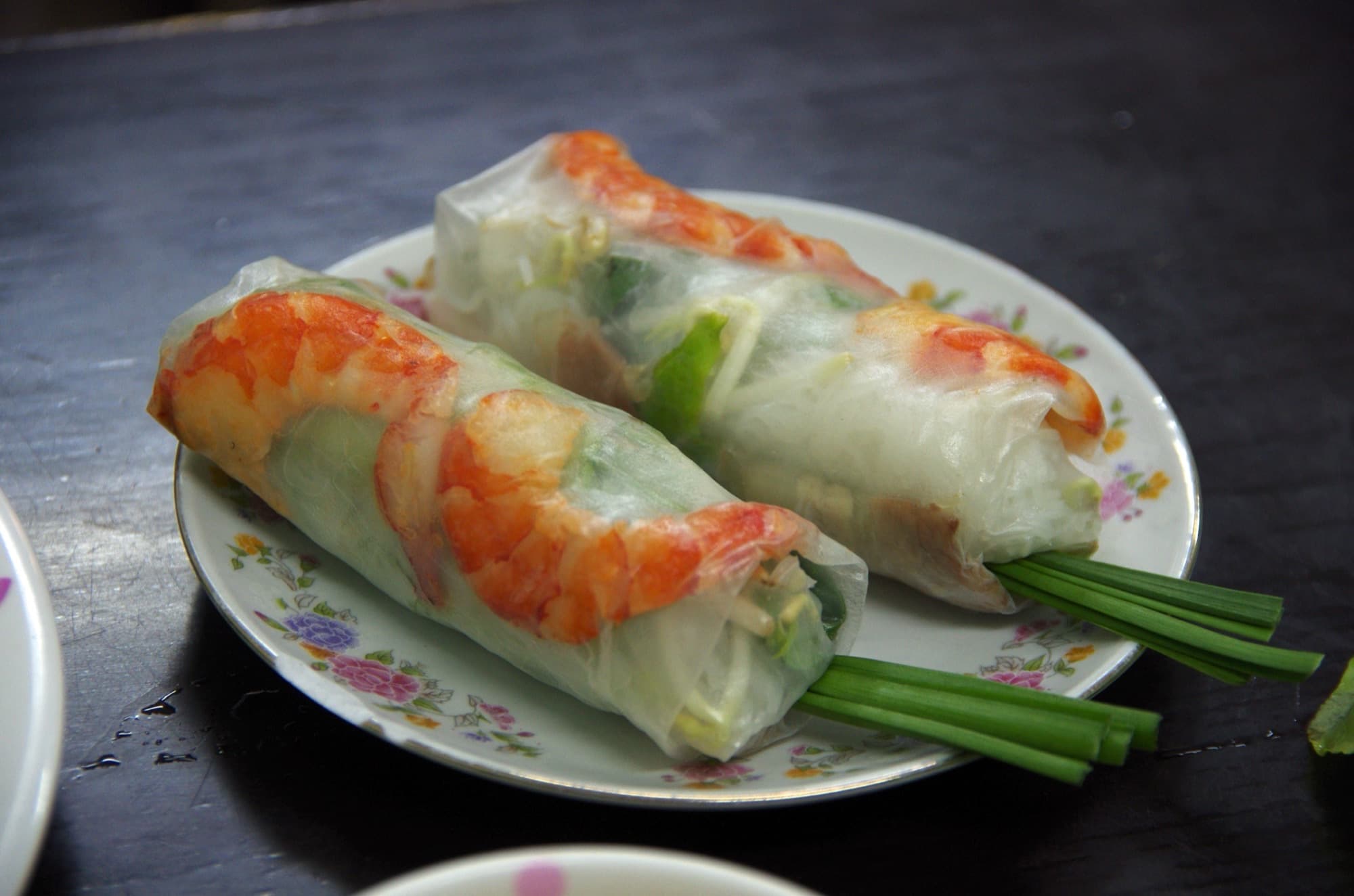 Two translucent Vietnamese summer rolls filled with shrimp, noodles, and herbs, with garlic chives sticking out