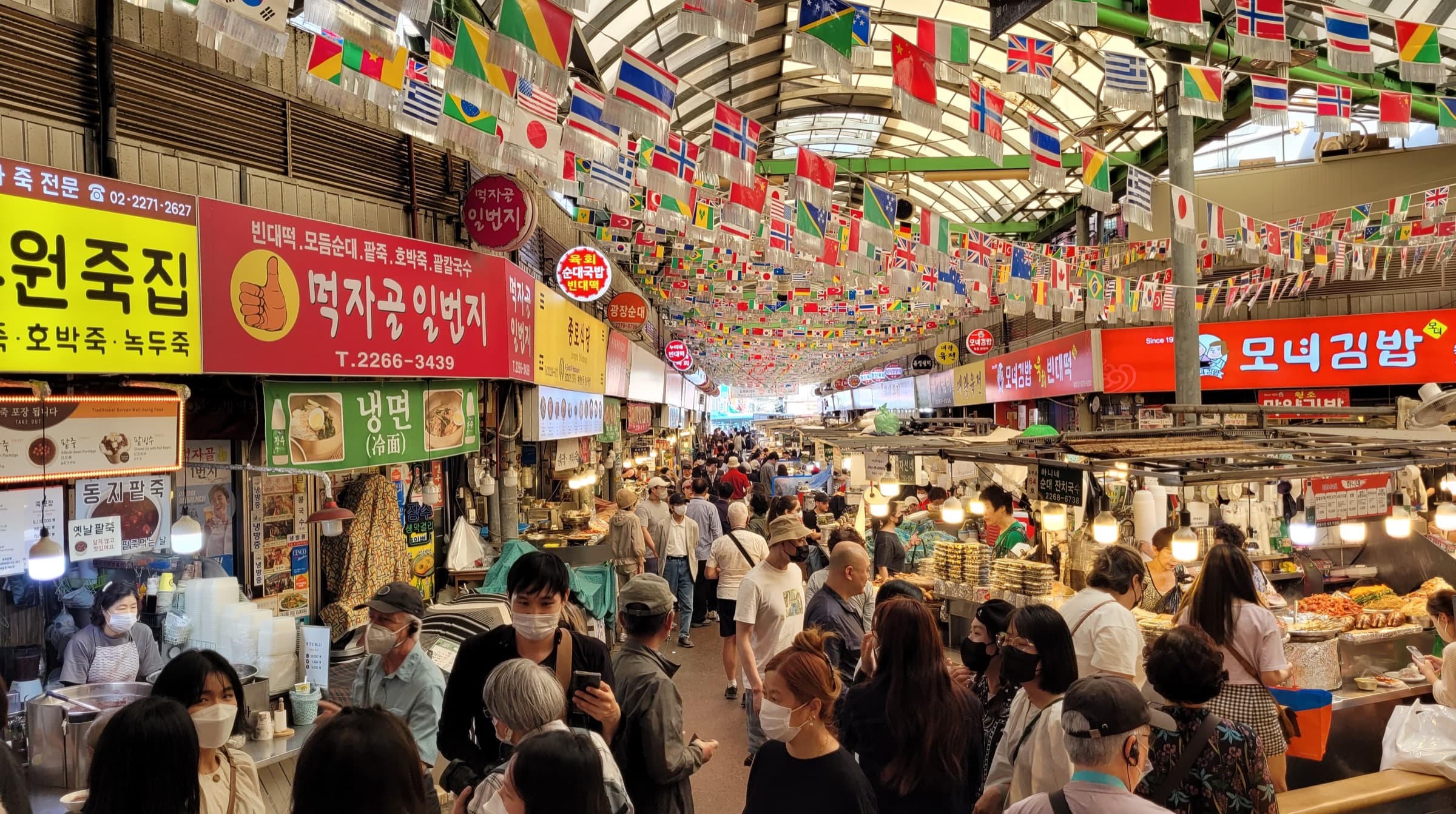 Gwangjang Market aisle with food stalls, flags, and morning light