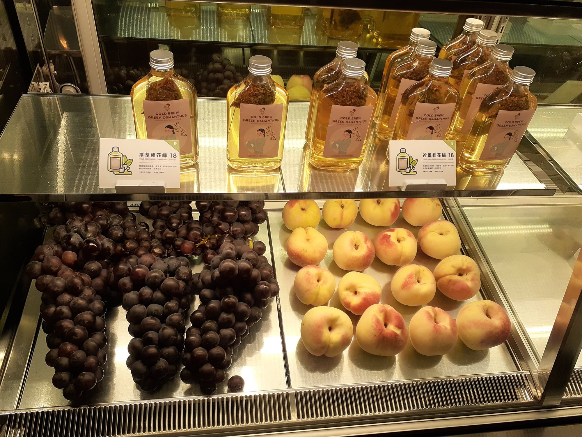 Glass case of Heytea cold-brew green osmanthus bottles above black grapes and white peaches