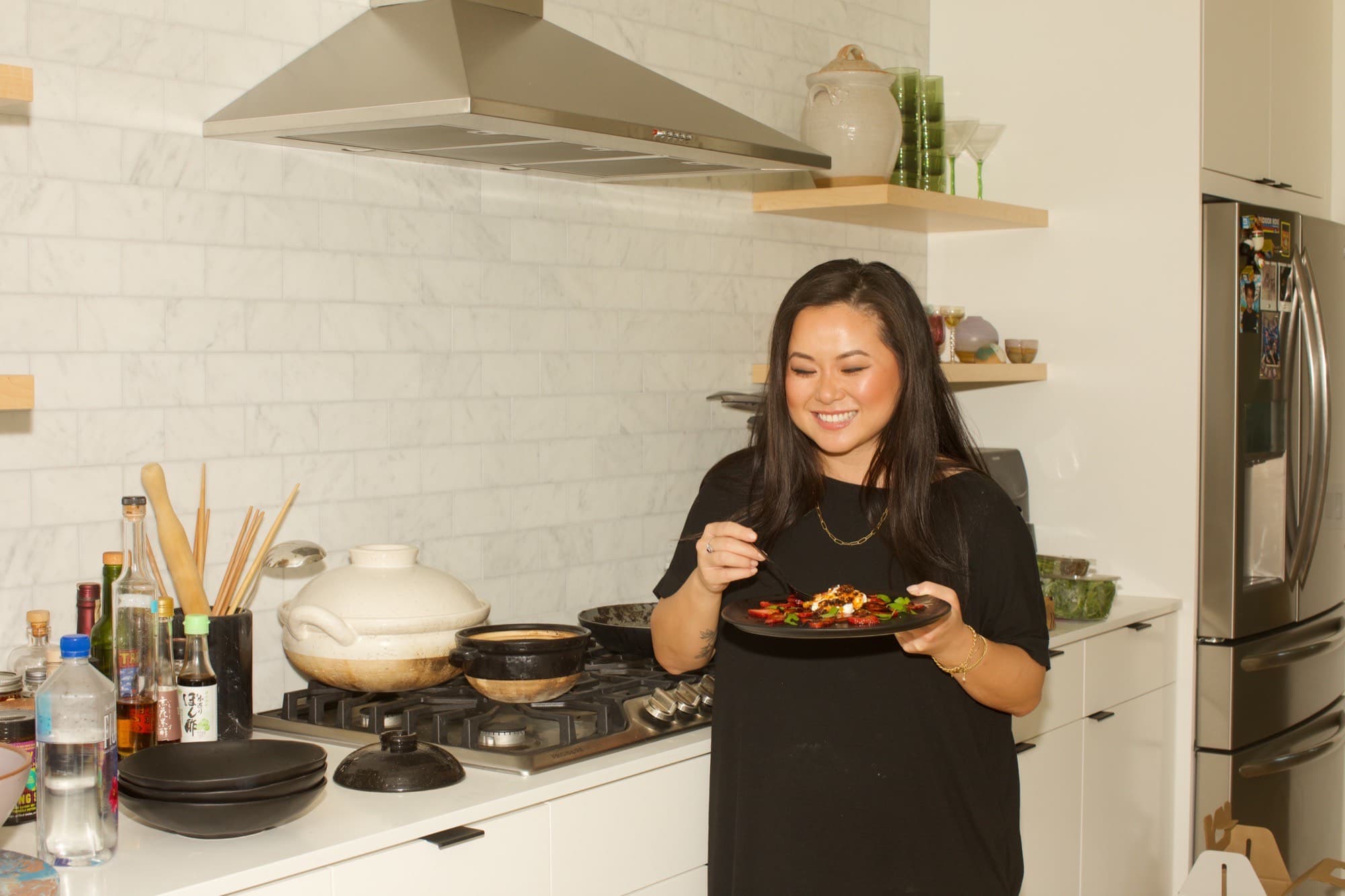 Jing Gao in a bright kitchen smiling at a plate of fruit finished with chili crisp