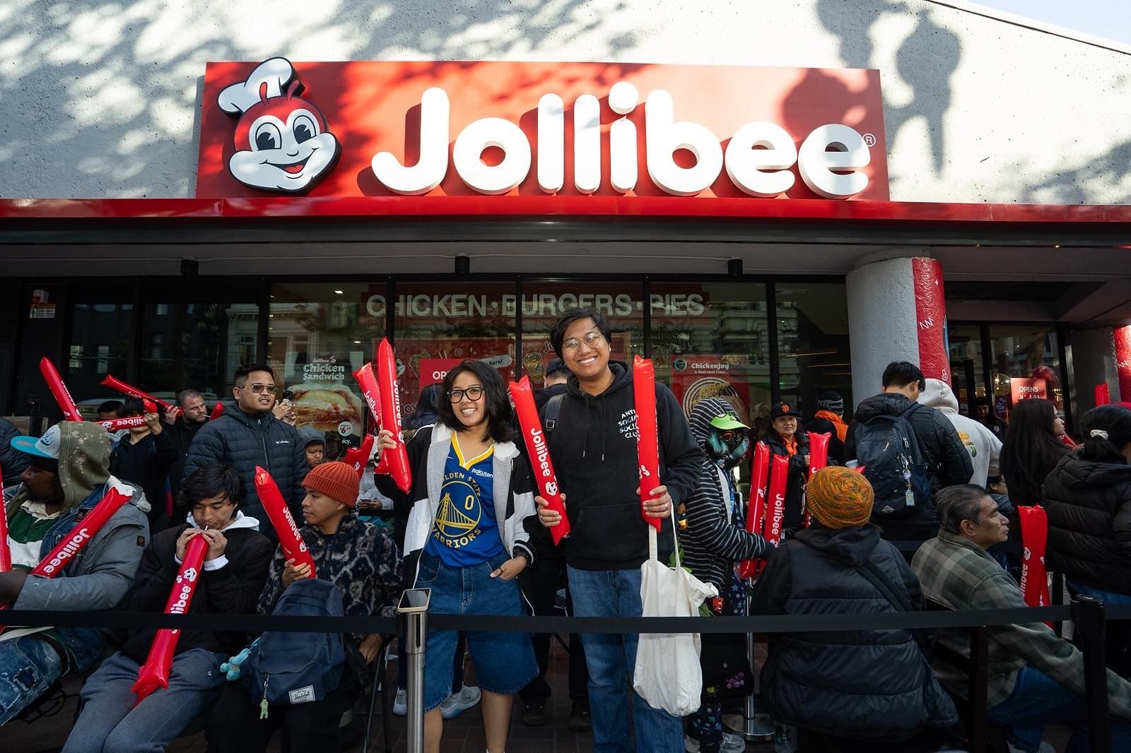 Crowds line up outside Jollibee on Market Street in downtown San Francisco on opening day, holding red Jollibee thundersticks under the storefront sign