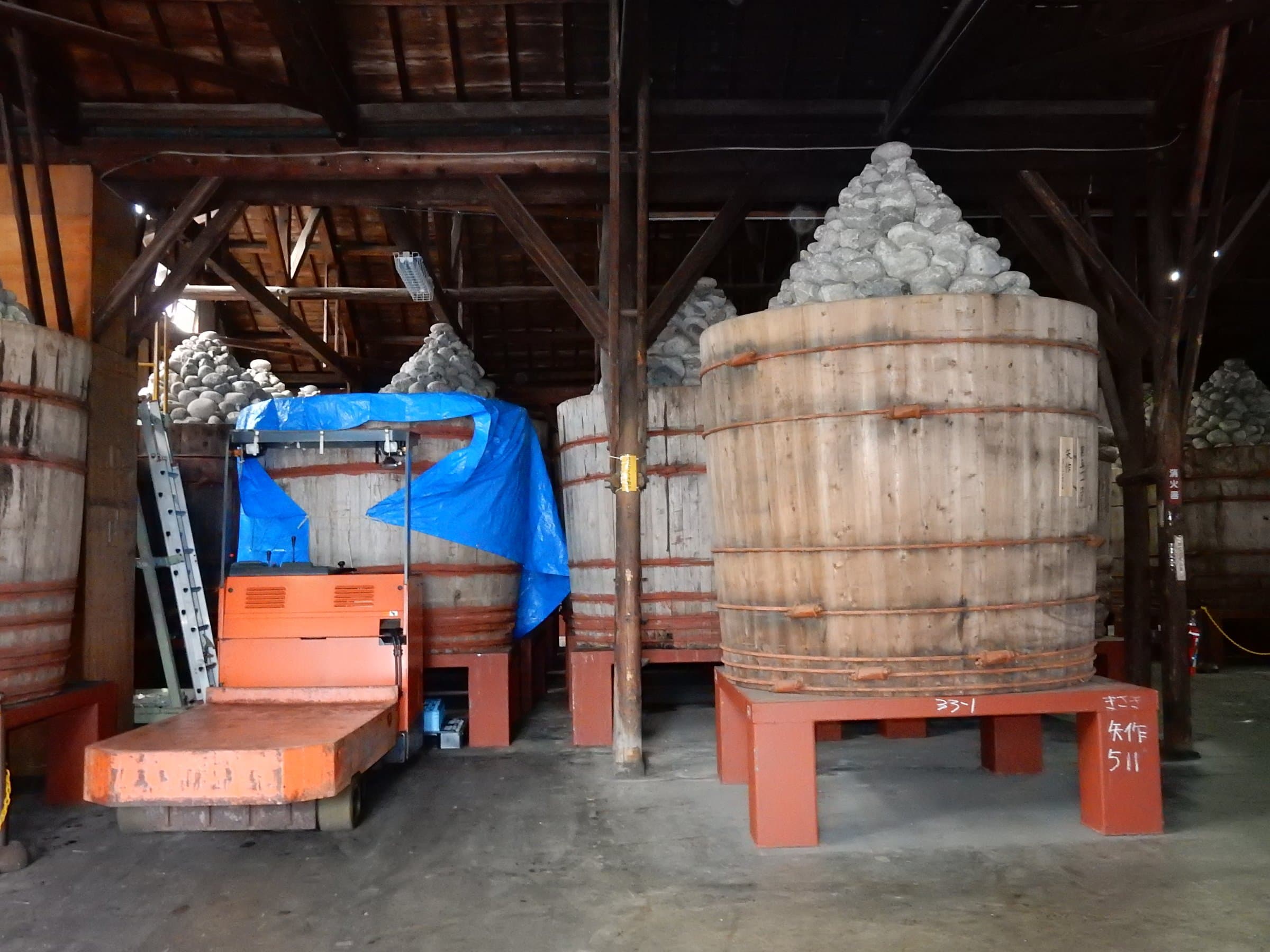 Cedar miso fermentation vats weighted with river stones in a traditional storehouse, Okazaki