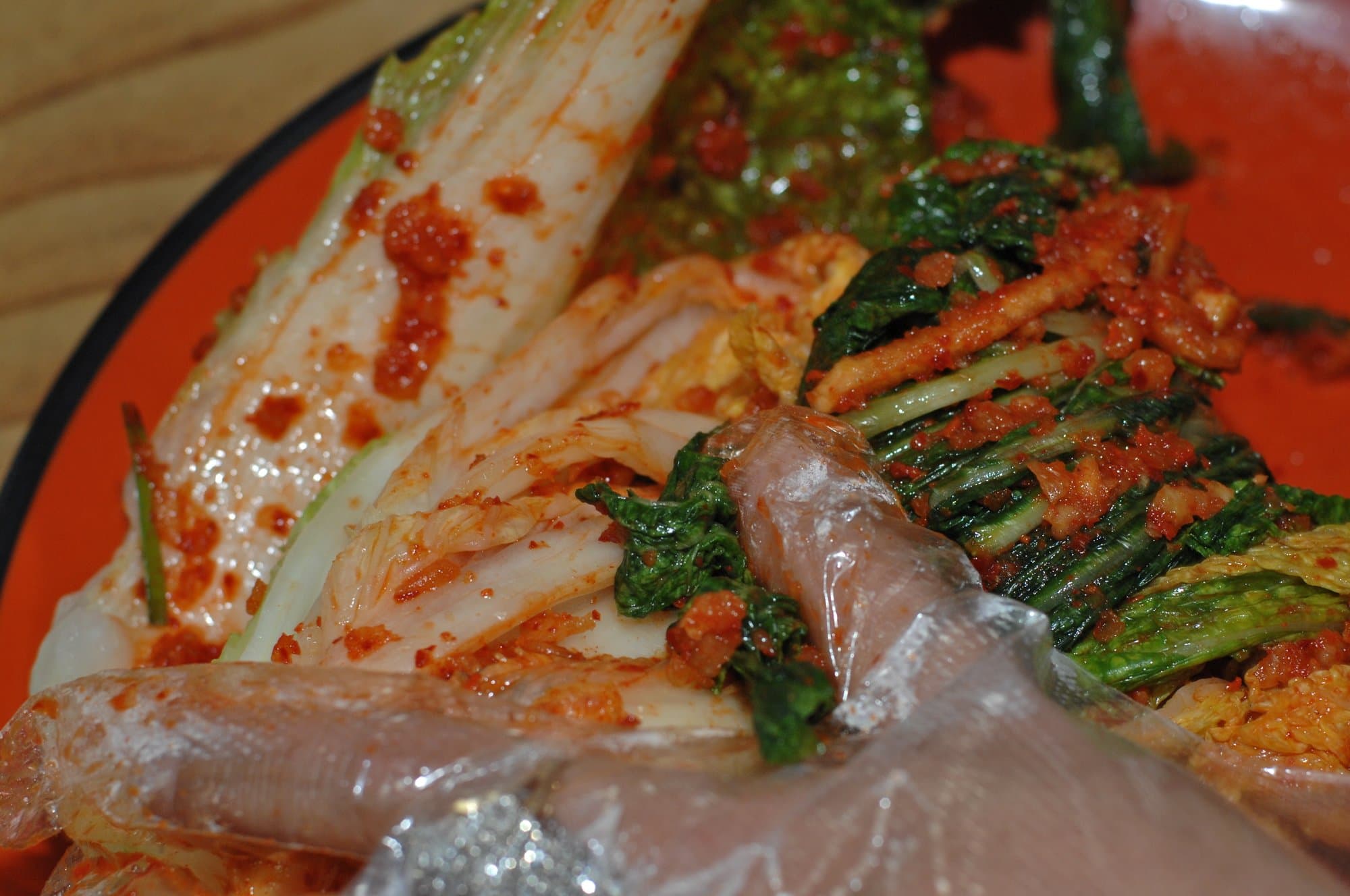 Gloved hands pressing red chile paste between the leaves of napa cabbage on an orange plate