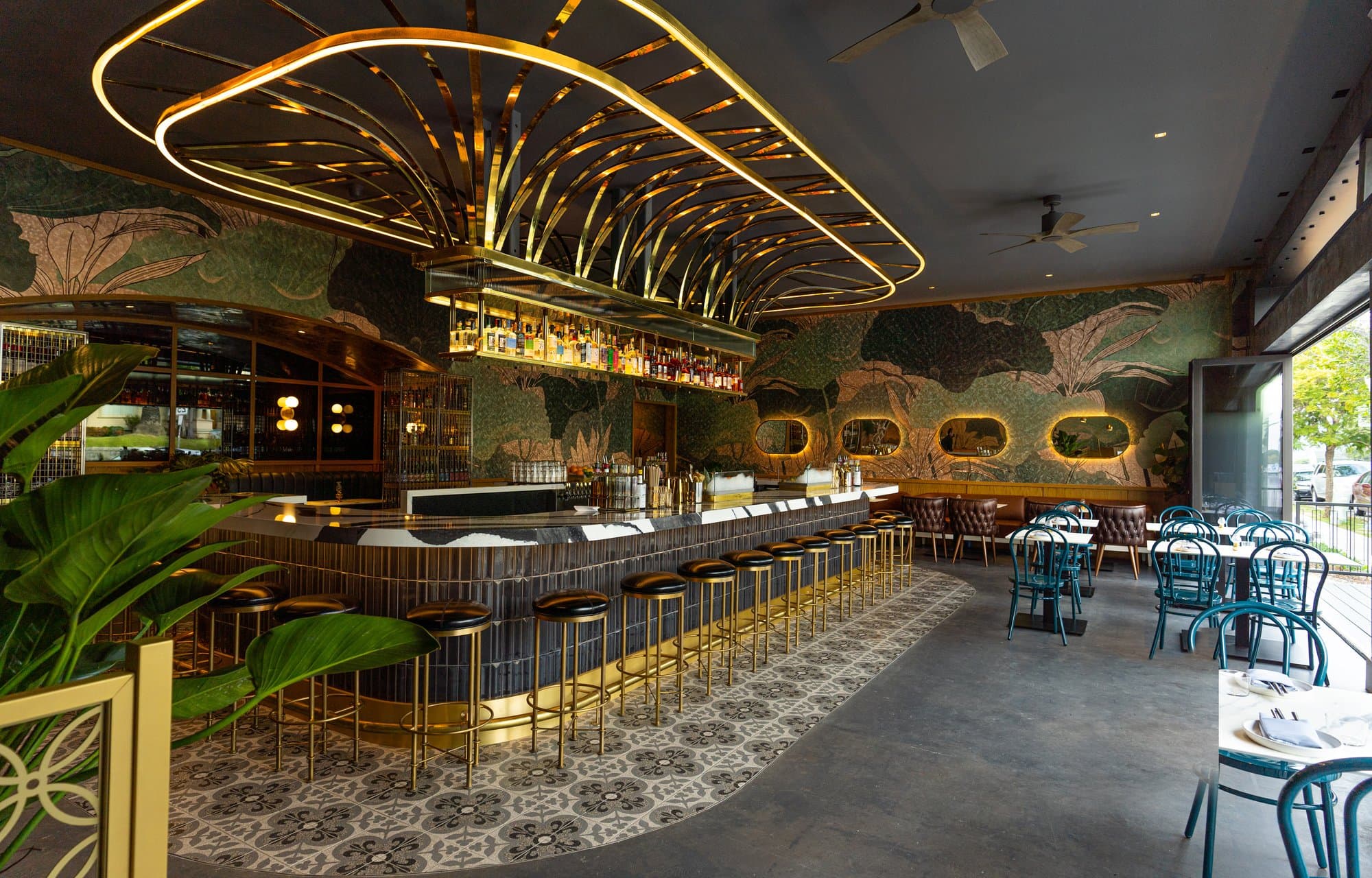 Kingfisher’s circular marble bar with brass stools under a curved metal canopy, lotus wallpaper and teal chairs in the Golden Hill dining room