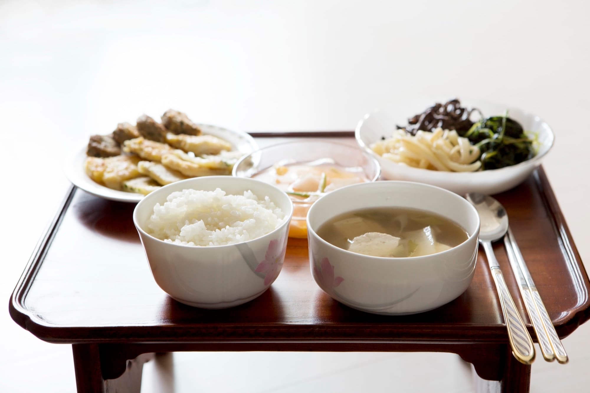 A Korean meal on a low wooden table with rice, tofu soup, seasoned vegetables, and pan-fried sides