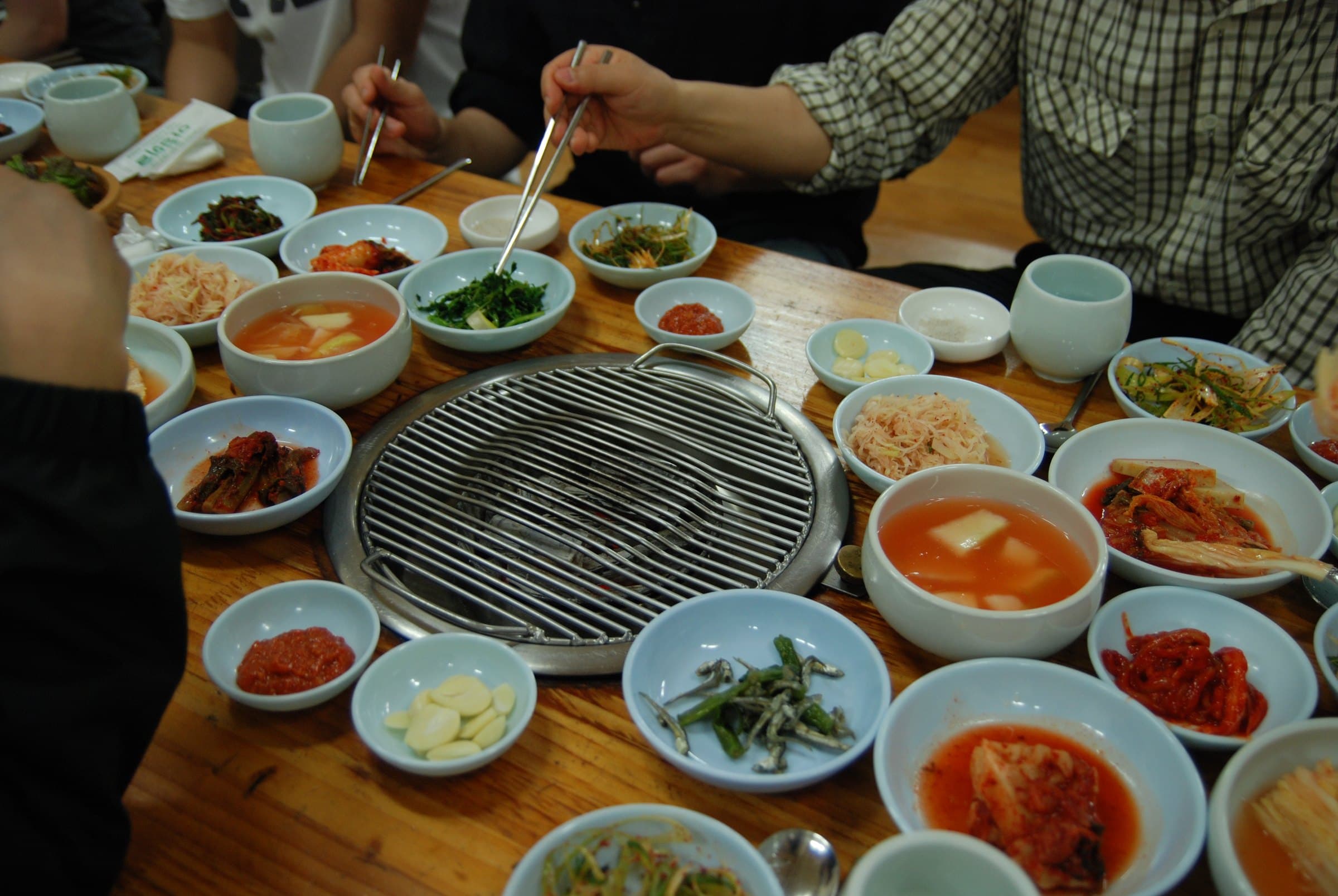 A tabletop Korean barbecue grill surrounded by bowls of banchan