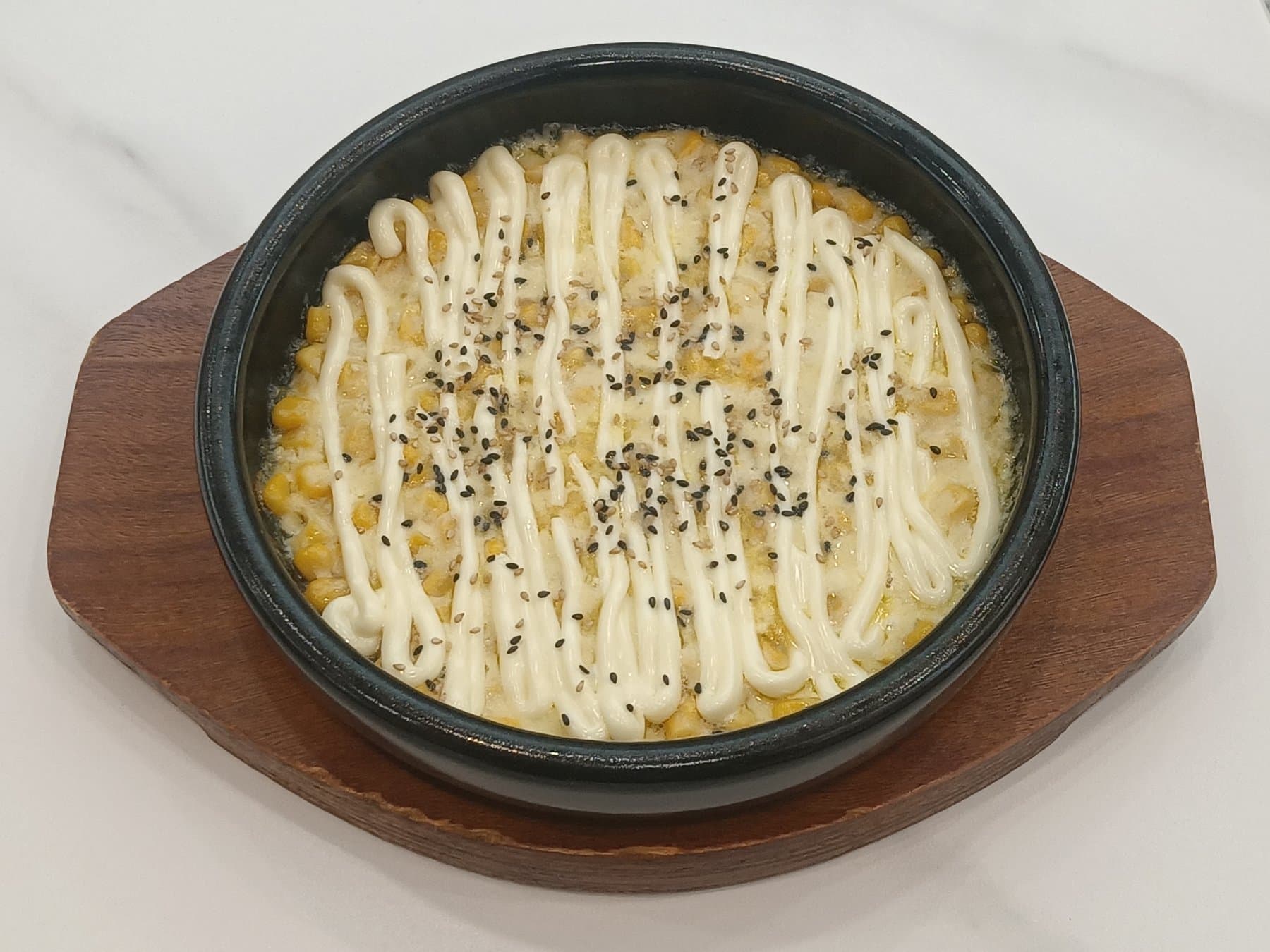 Bubbling Korean corn cheese in a black skillet, topped with mayonnaise and sesame seeds