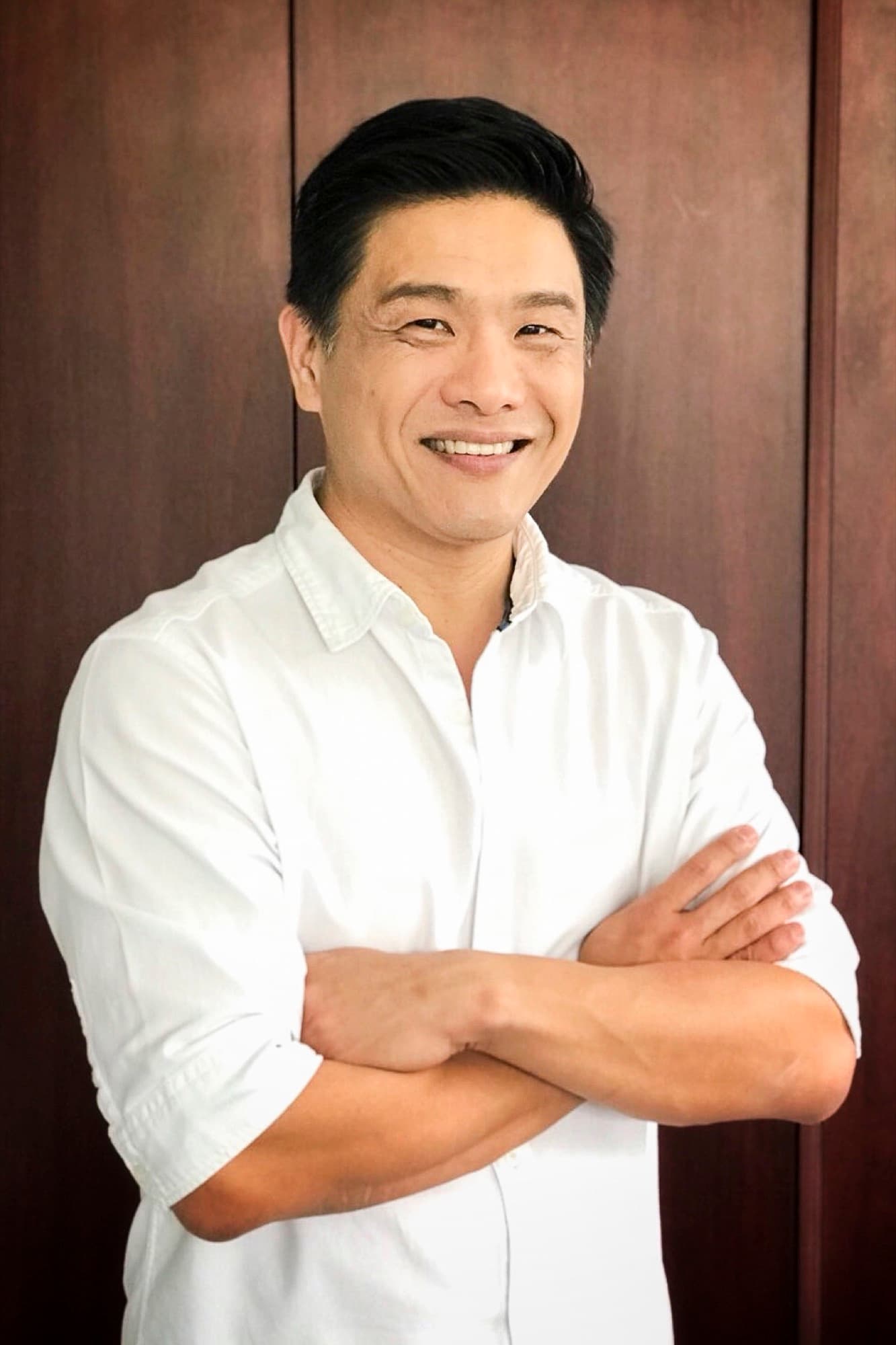 Dr Leslie Tay smiling with arms crossed in a white shirt