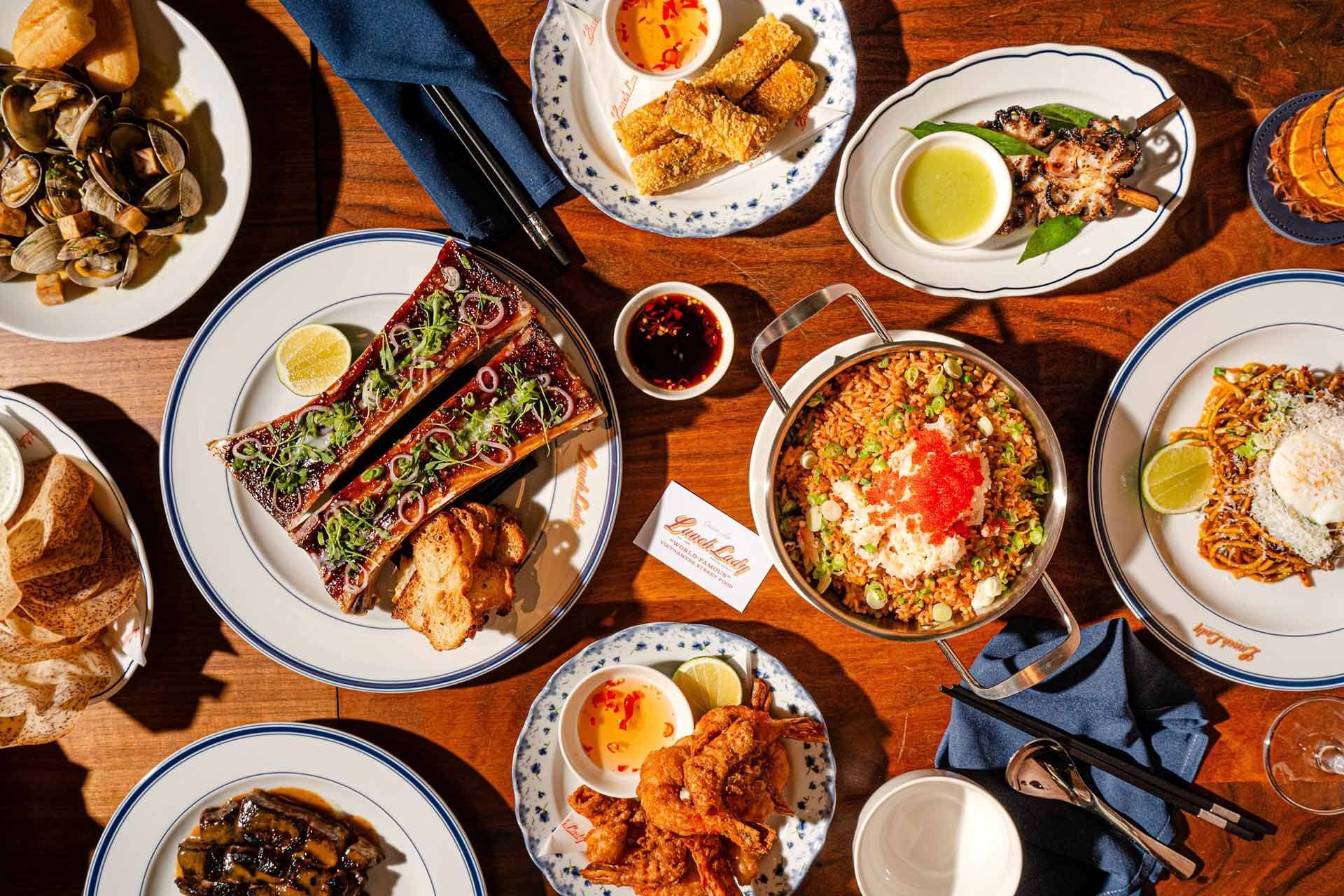 Overhead of a crowded Lunch Lady table with short rib, crab fried rice, fried prawns, octopus, and garlic noodles