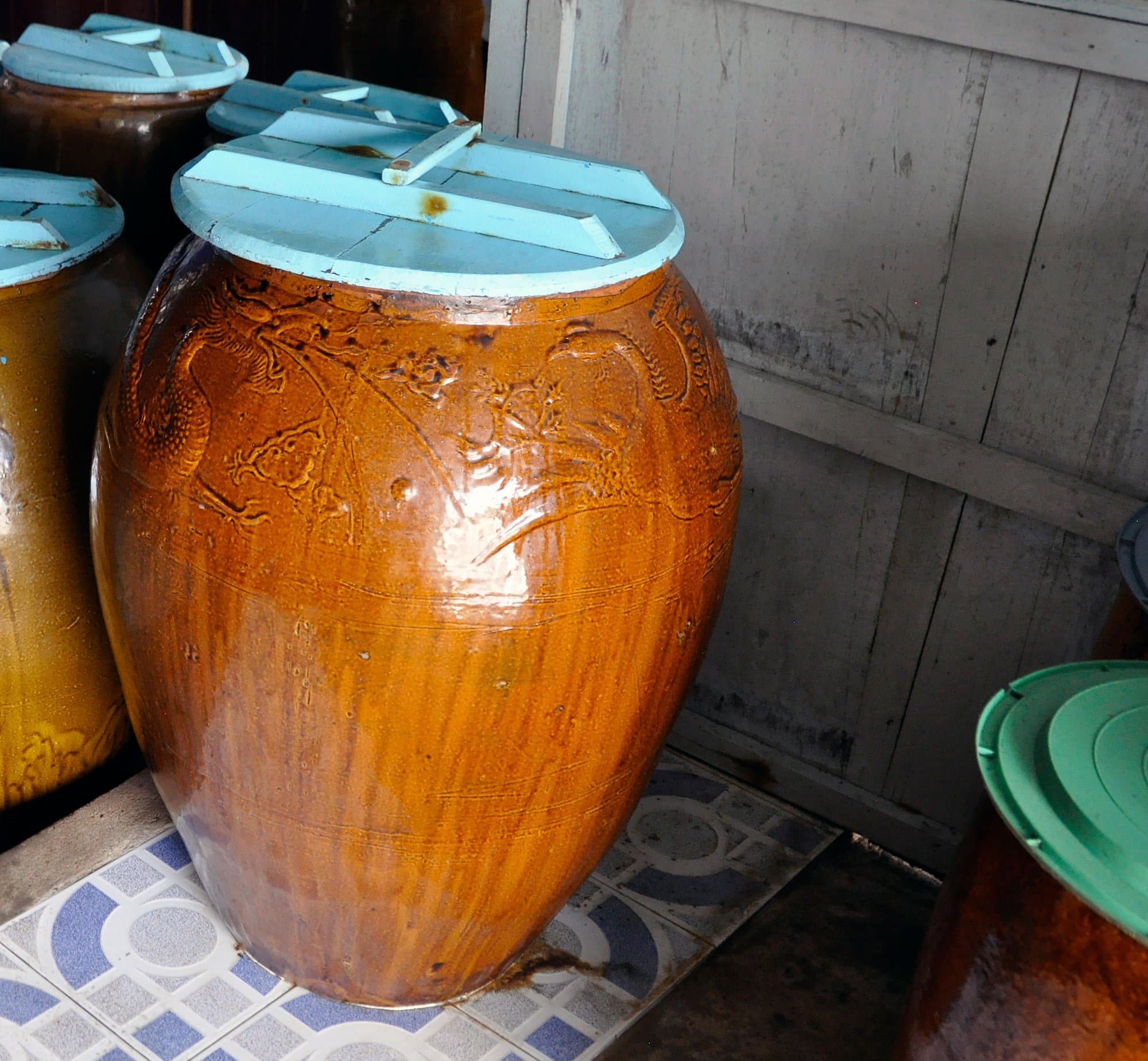 Glazed ceramic jars with pale blue lids in a fish-sauce workshop, the front jar carved with a dragon