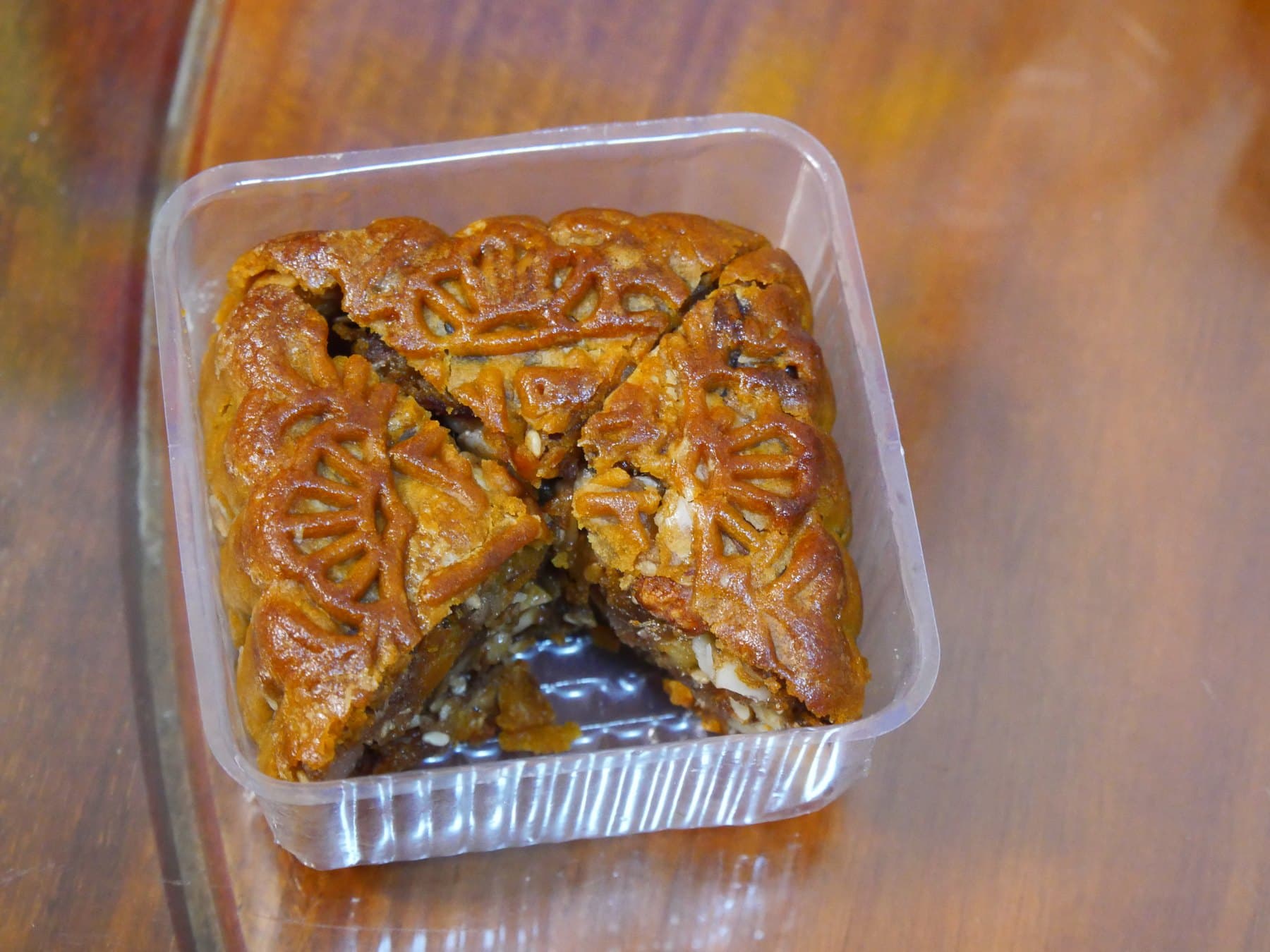 A golden five-nut mooncake cut into wedges in a clear plastic tray, dense nut filling visible