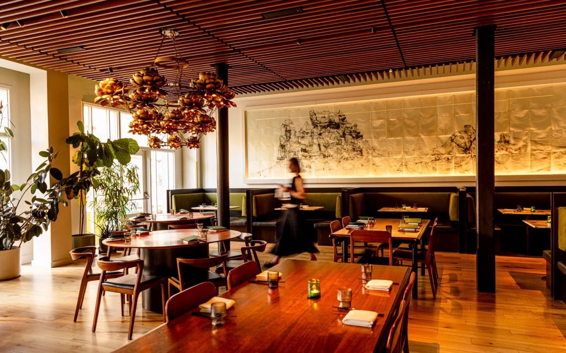 The main dining room at Mister Jiu’s in San Francisco Chinatown, with a gold lotus chandelier over polished wood tables
