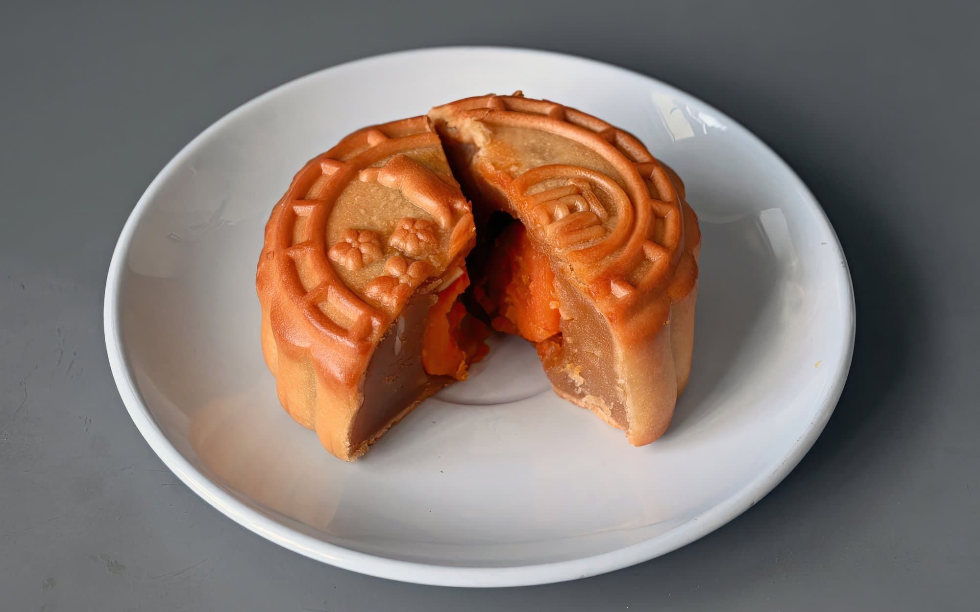 Cantonese mooncake cut open to show lotus seed paste and salted egg yolk on a white plate