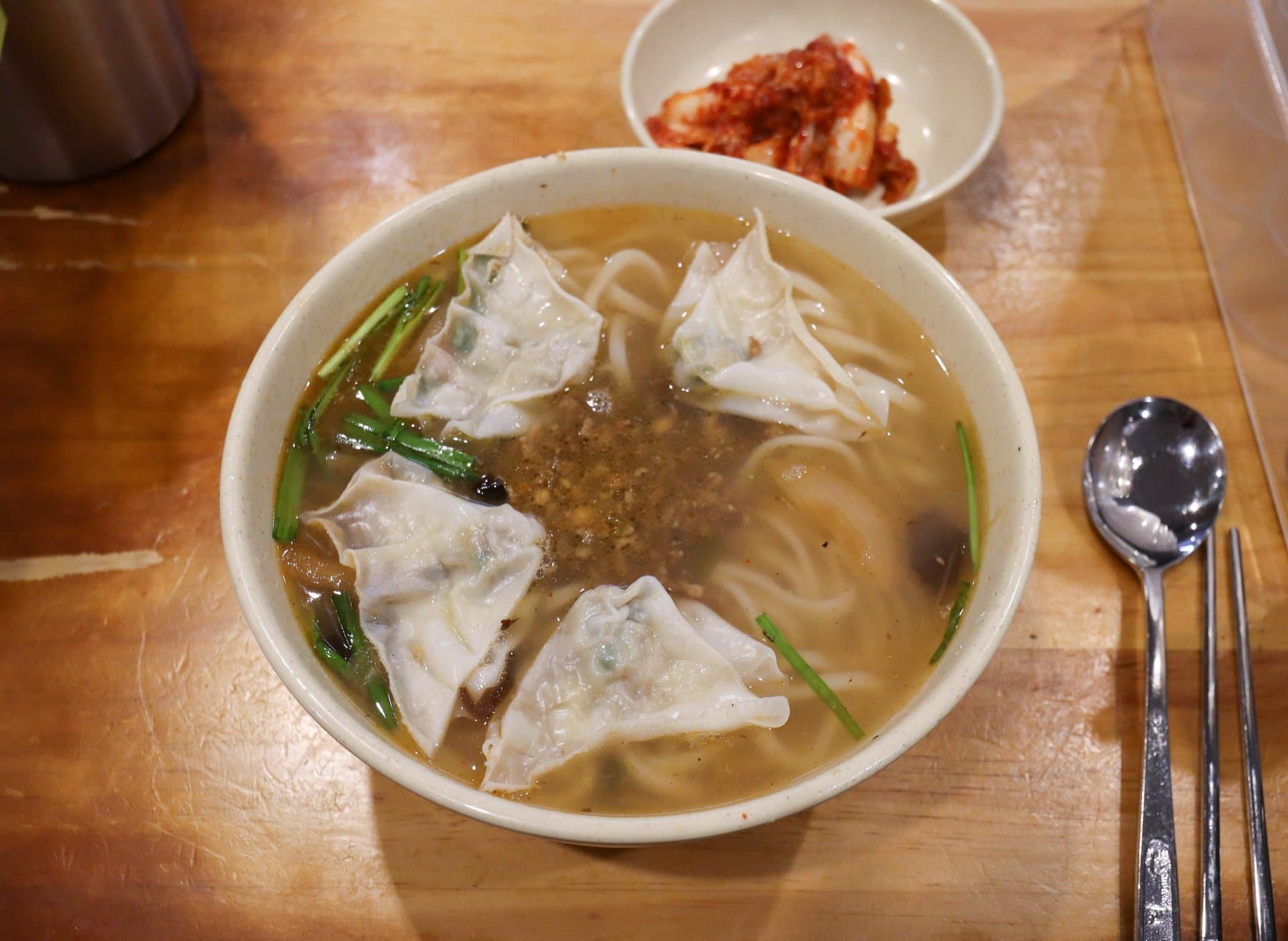 Ceramic bowl of kalguksu noodles and dumplings with kimchi and metal chopsticks at Myeongdong Kyoja