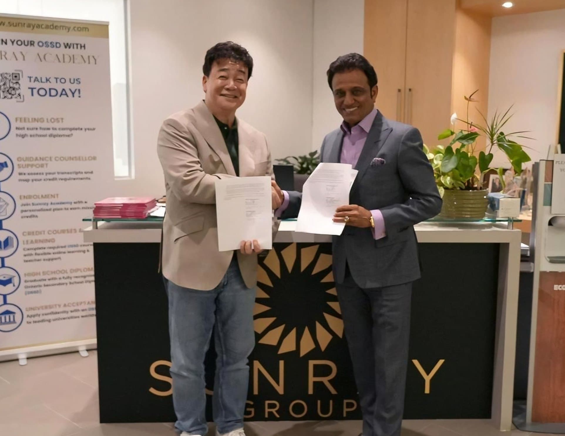 Paik Jong-won and Sunray Group CEO Rattan Gupta shaking hands and holding signed documents behind a Sunray Group reception desk