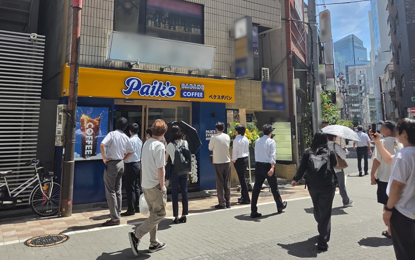 Paik’s Coffee Tokyo storefront with yellow Dabang Coffee sign and office workers in line
