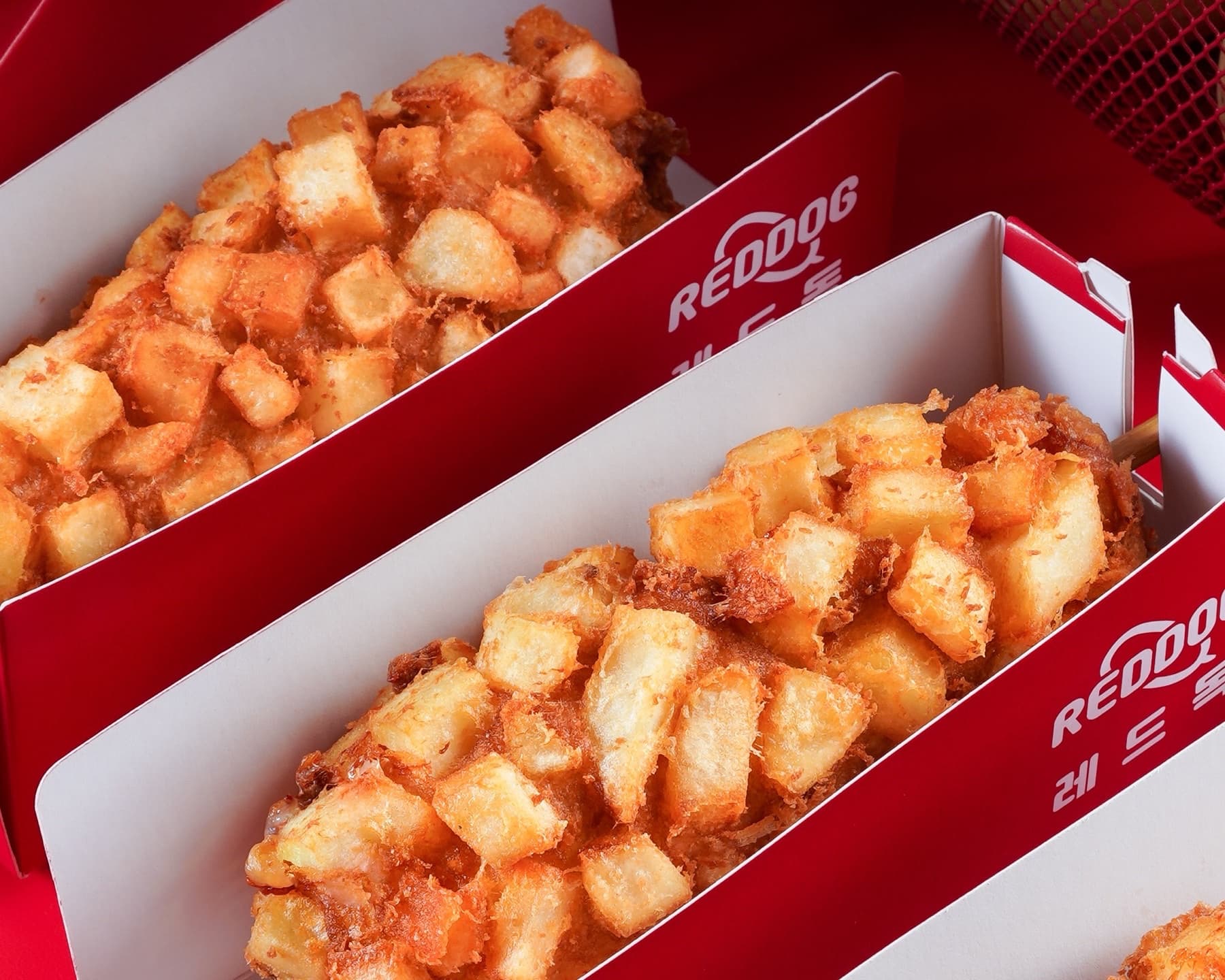 Golden Korean potato corn dogs in Reddog red boxes, one cut open to show the filling
