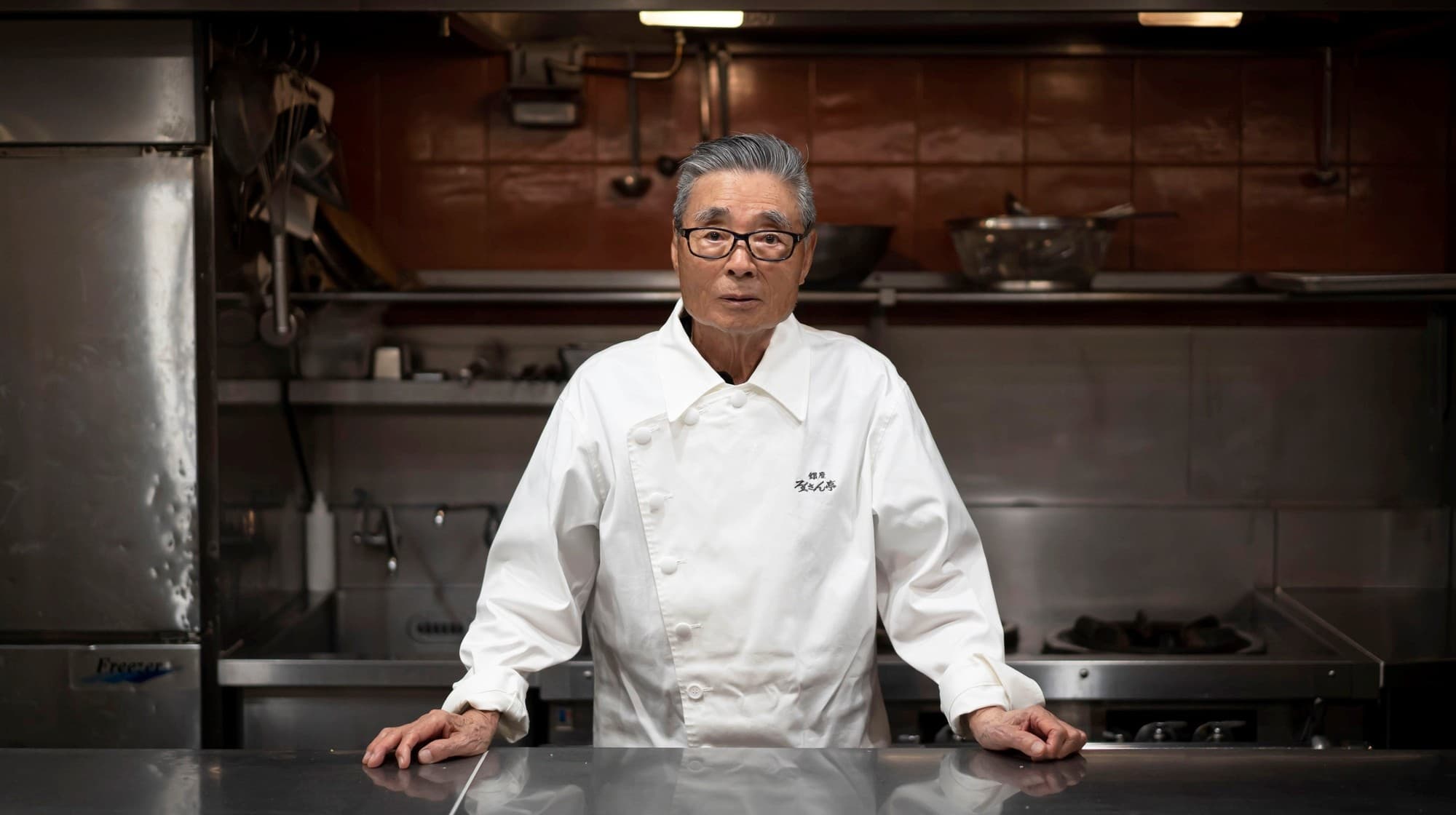 Rokusaburo Michiba in a white chef coat standing at a stainless steel kitchen counter