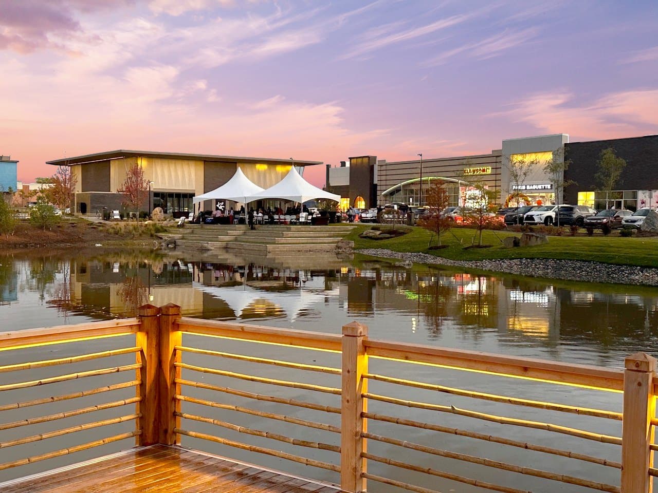Dusk plaza and pond at Sakura Novi with Paris Baguette and storefront lights across the water