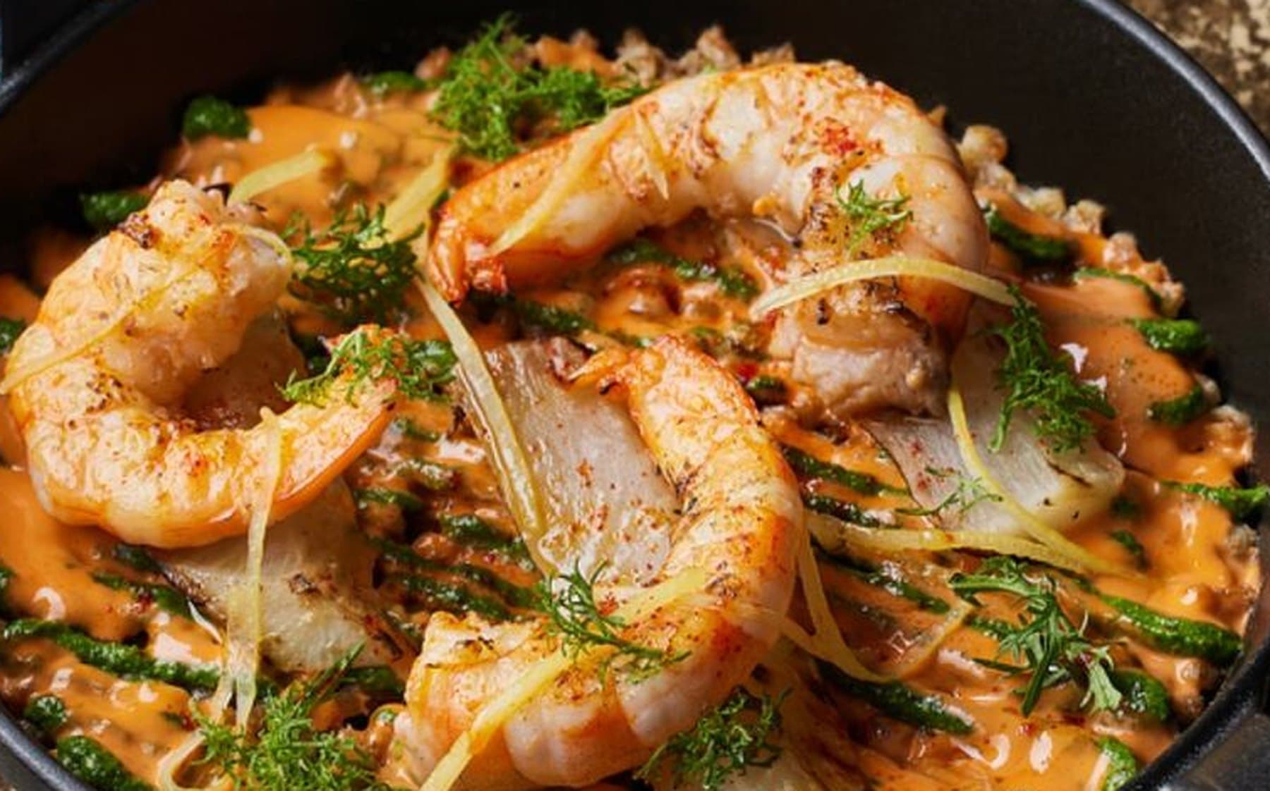 Shrimp and grains in a black cast-iron skillet with orange sauce and green herb oil at Sapid Seoul