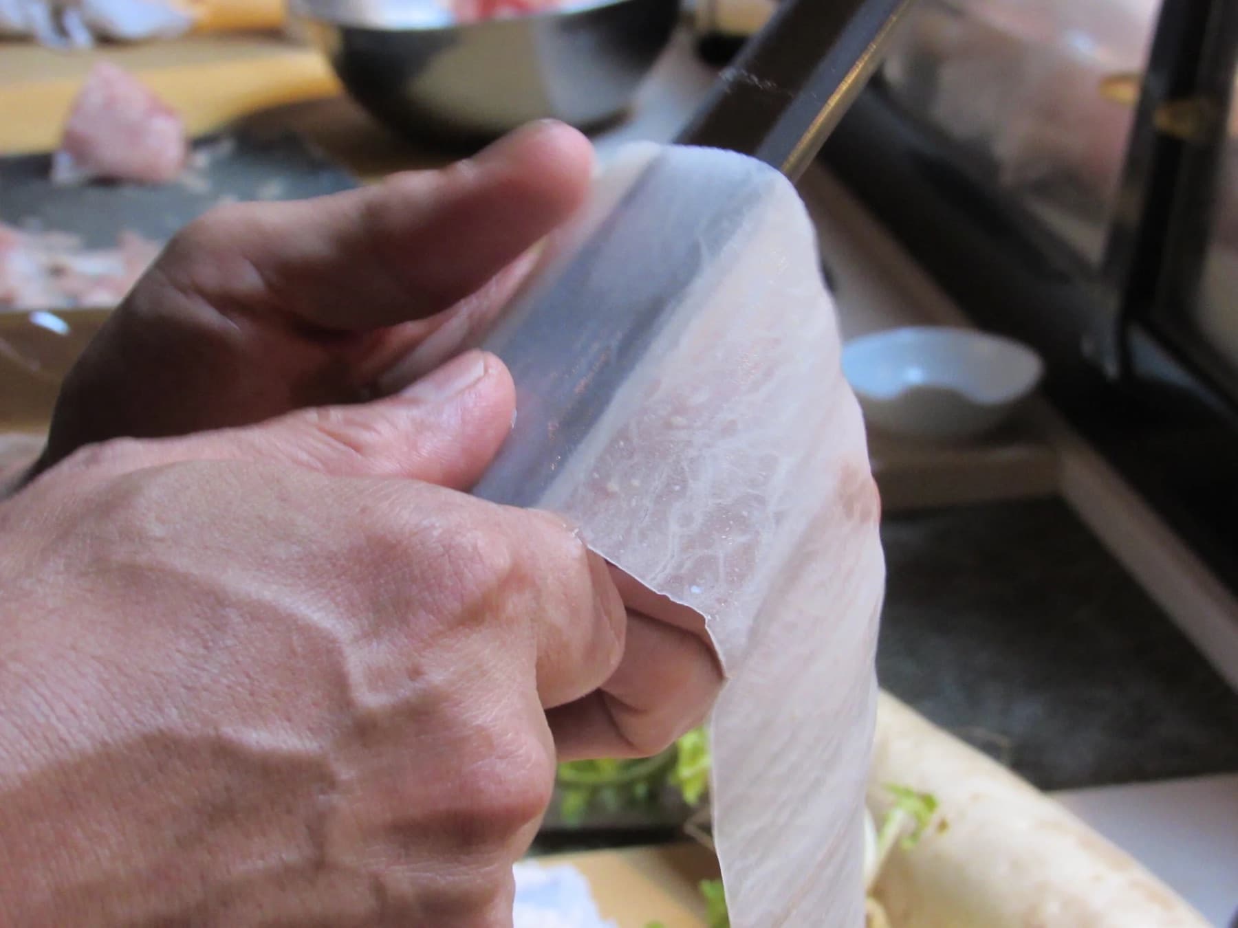 Chef hands rotary-peeling a paper-thin sheet of daikon with a Japanese vegetable knife