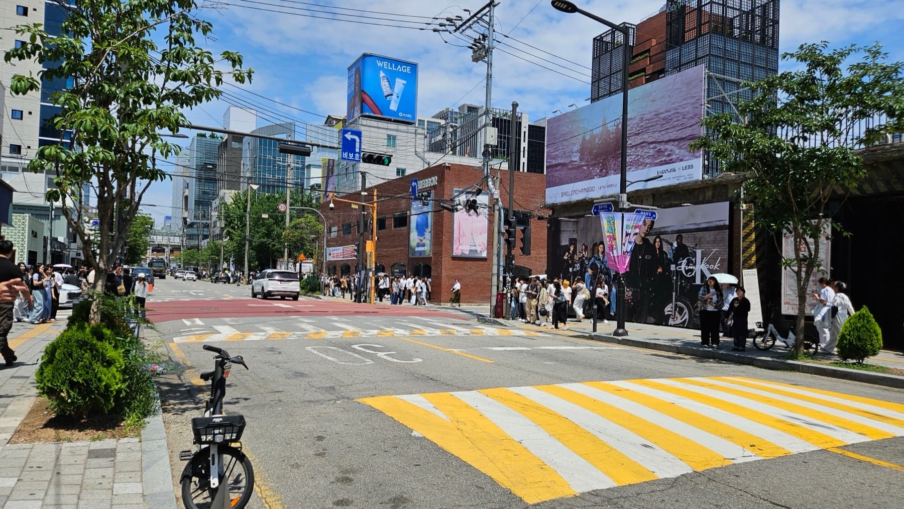A busy Seongsu-dong intersection with red-brick warehouses, fashion billboards, and people queued along the sidewalk