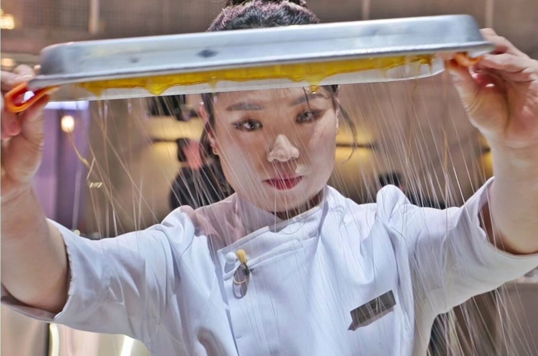Chef Jung Ji-sun lifting a tray as golden sugar threads fall in front of her