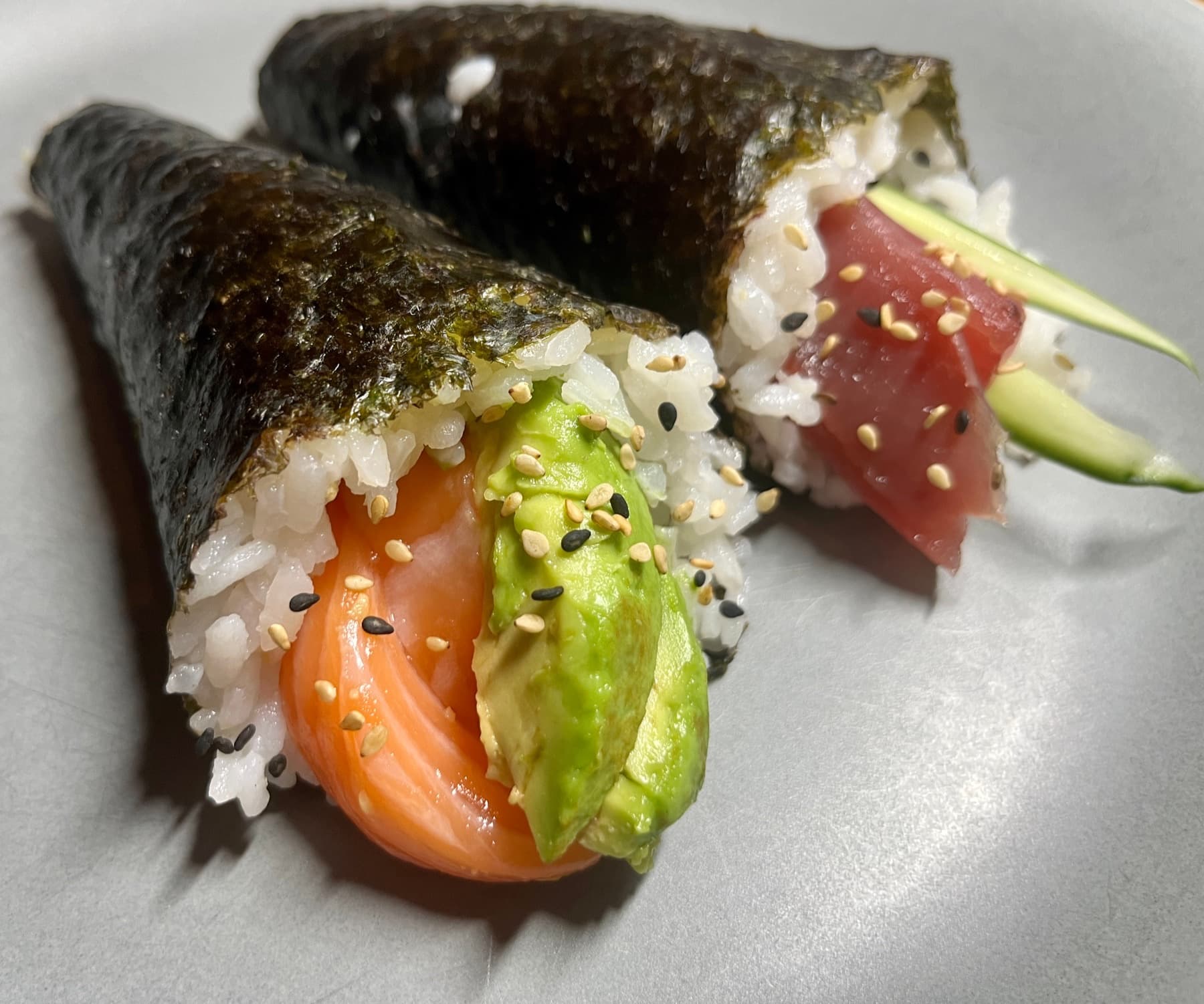 Two temaki hand rolls on a plate, salmon-avocado and tuna-cucumber