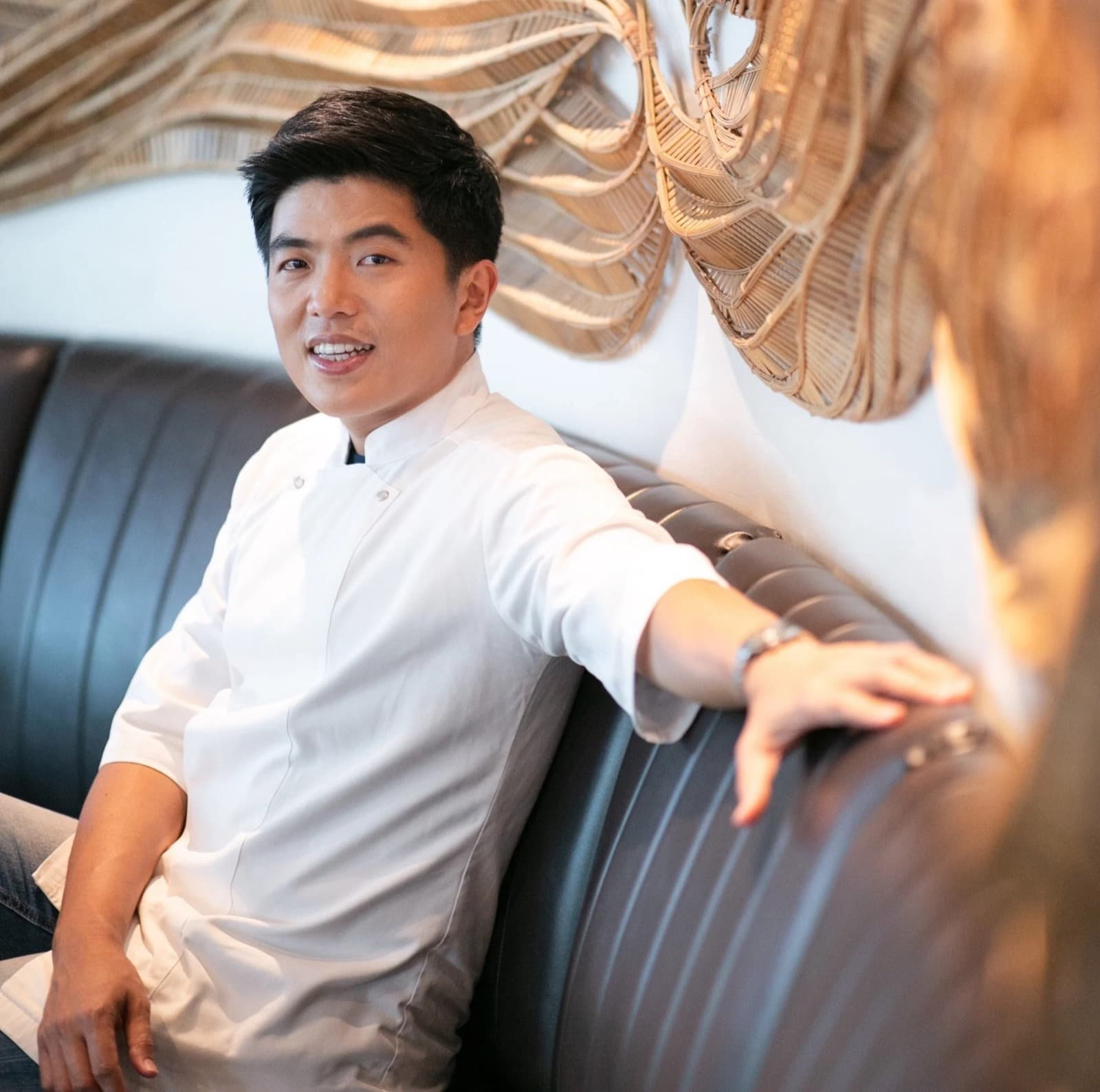 Chef Thitid Ton Tassanakajohn in a white chef’s jacket seated in a restaurant