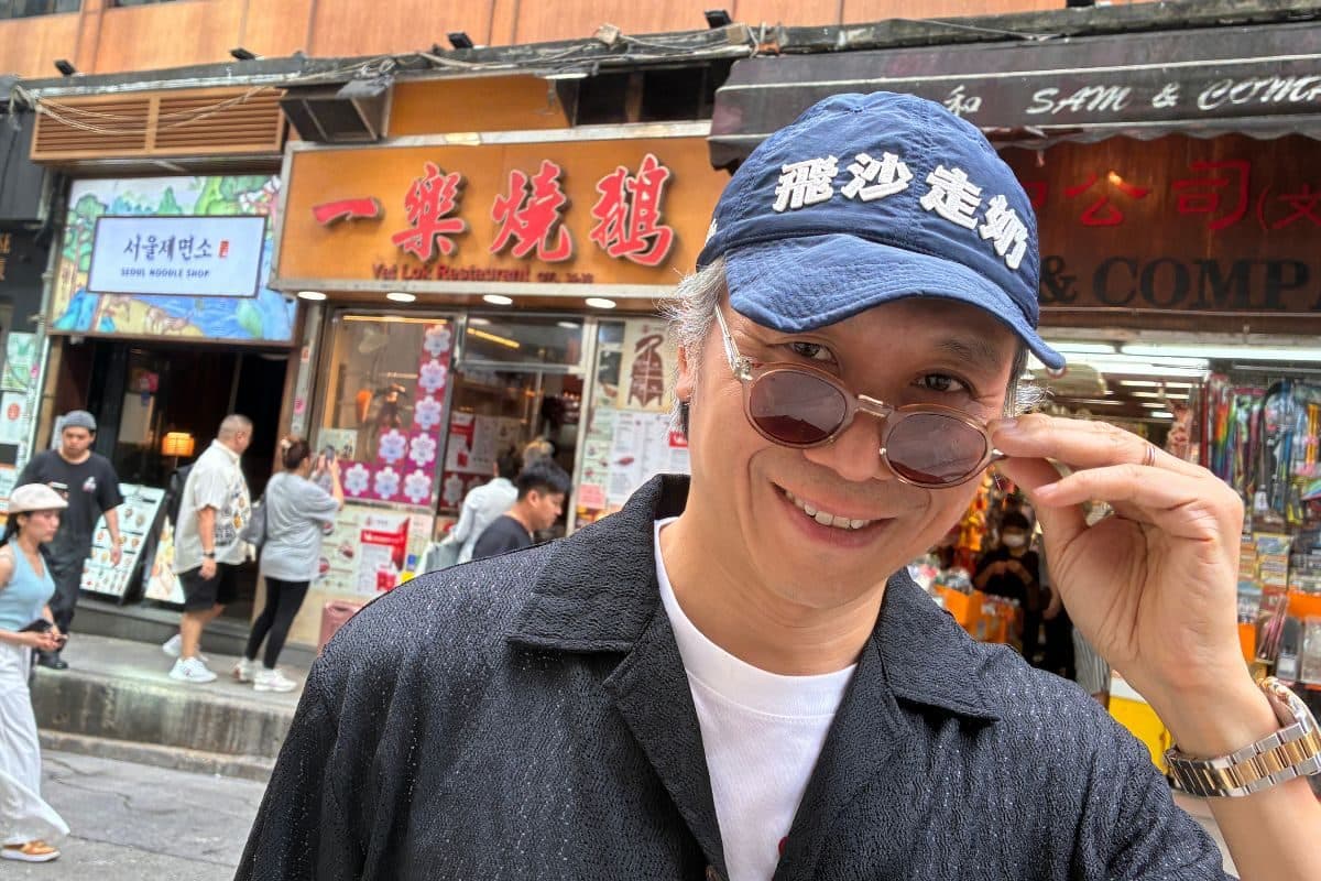 Kent Wong, known as Uncle K, smiling in a baseball cap and sunglasses on a Hong Kong street