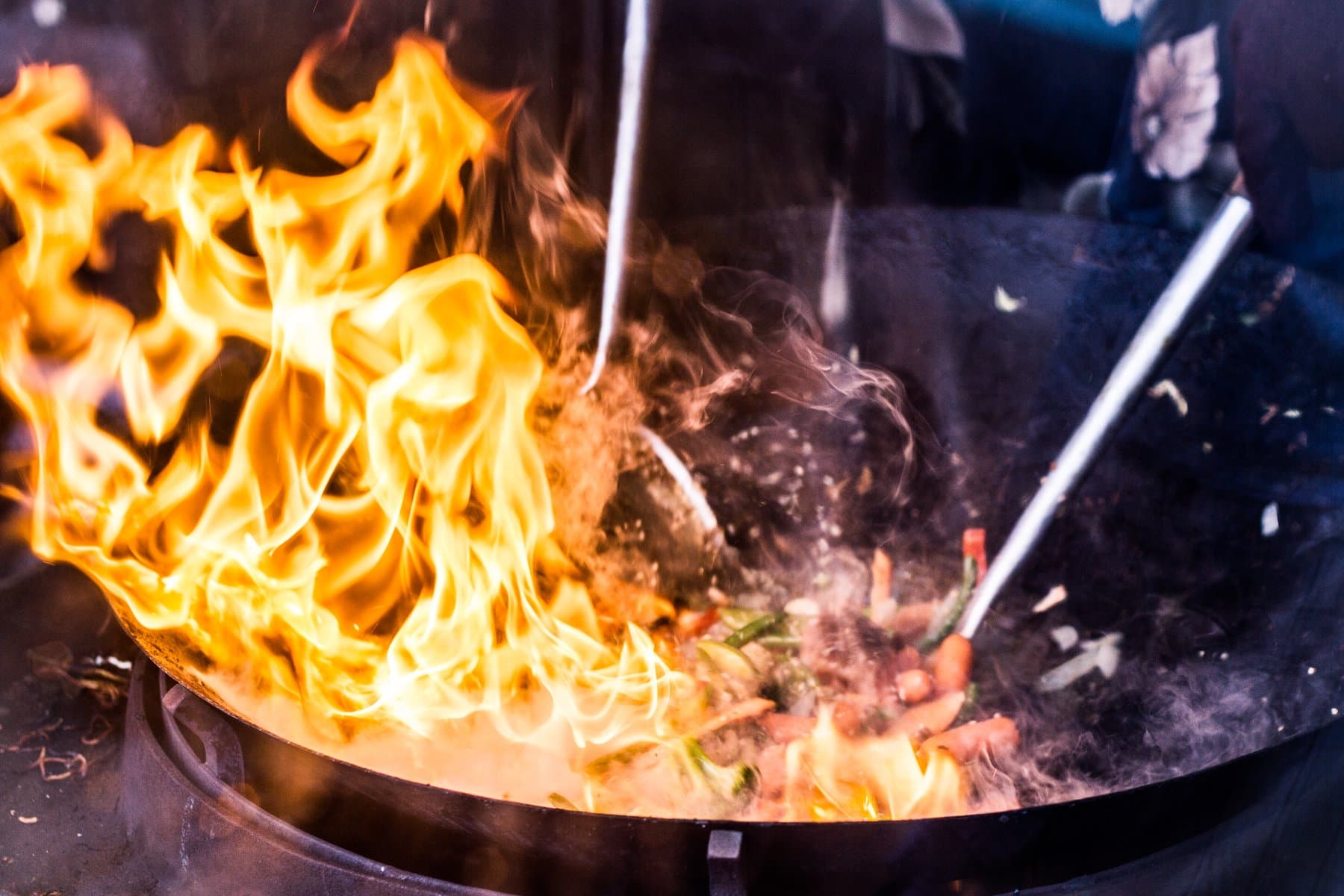Vegetables tossing in a wok with bright flames rising from a high-heat burner