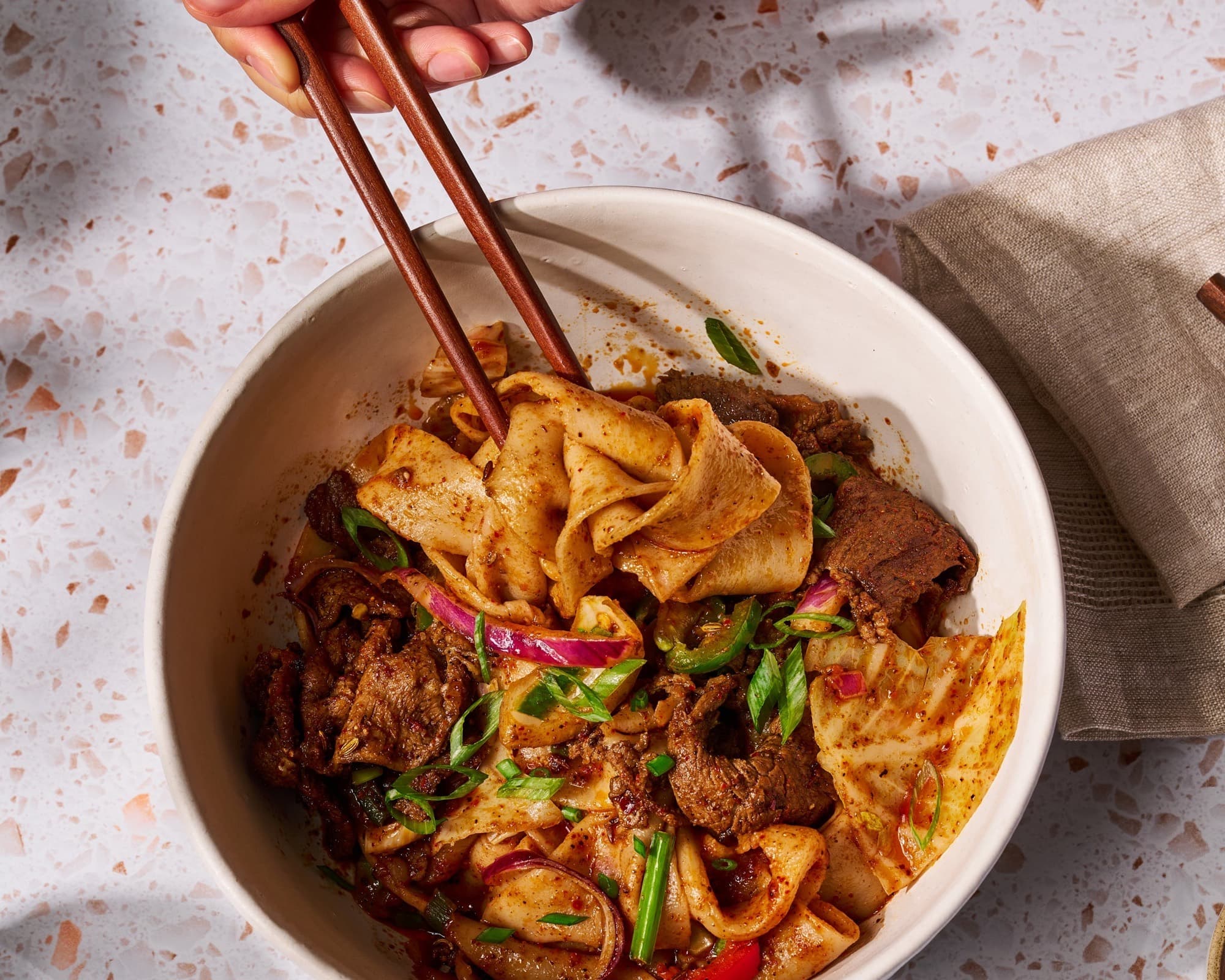 Bowl of spicy cumin lamb hand-ripped noodles with chili oil and scallions