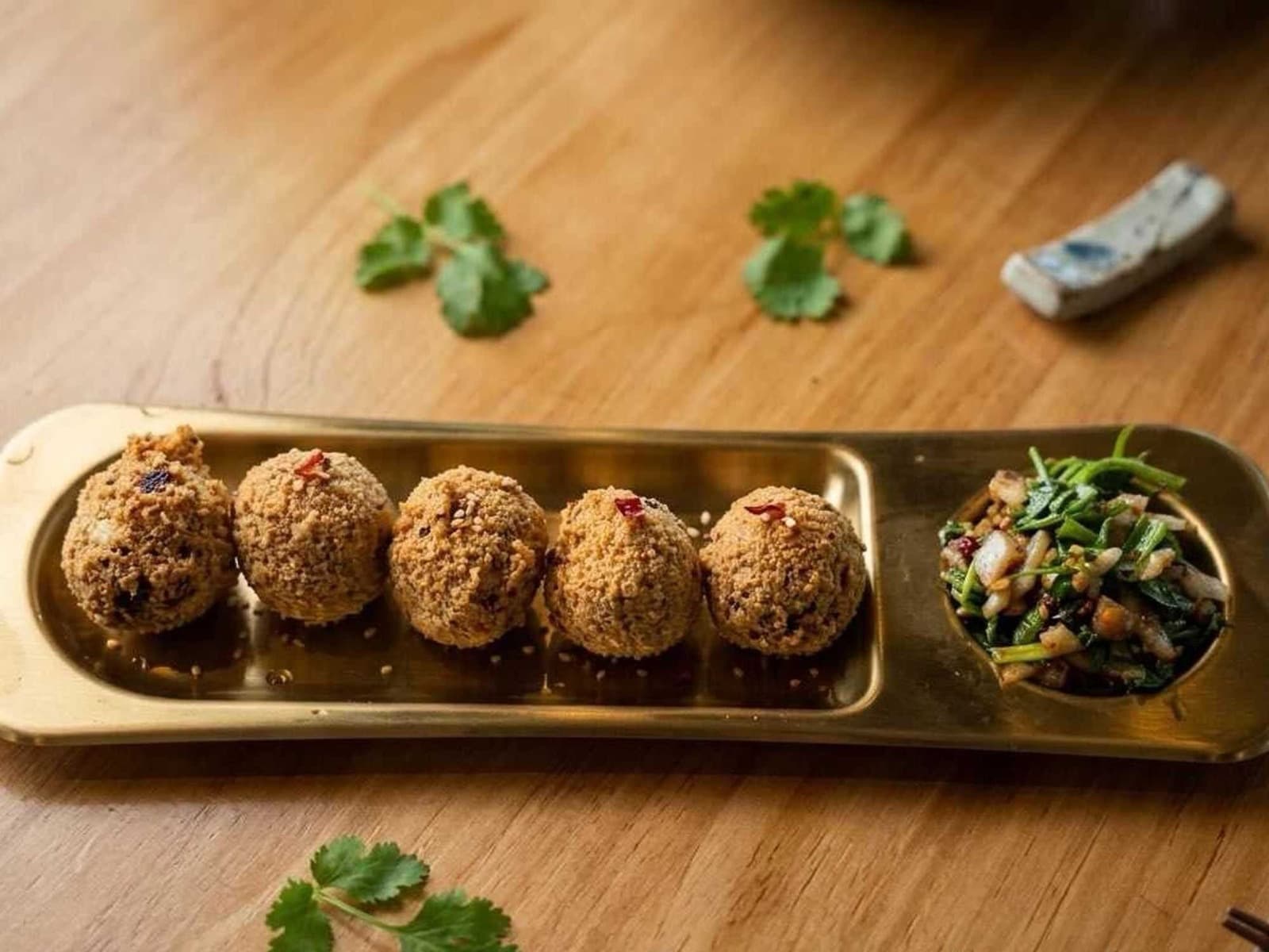 Crispy Guizhou tofu balls on a gold tray with greens and cilantro